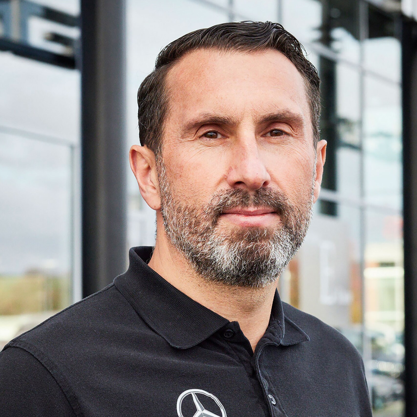 Automobilfachmann im Firmen-Poloshirt vor Gebäude eines Mercedes-Benz Partnerbetriebs 