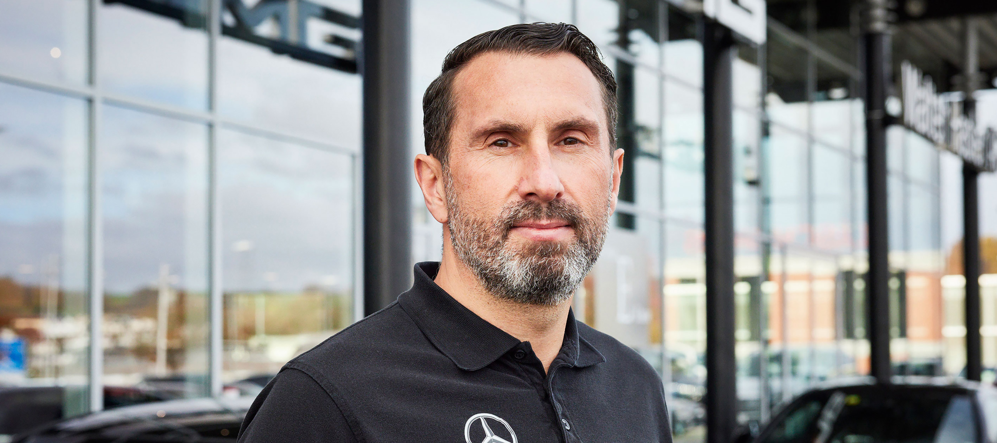 Automobilfachmann im Firmen-Poloshirt vor Gebäude eines Mercedes-Benz Partnerbetriebs Automobilfachmann im Firmen-Poloshirt vor Gebäude eines Mercedes-Benz Partnerbetriebs