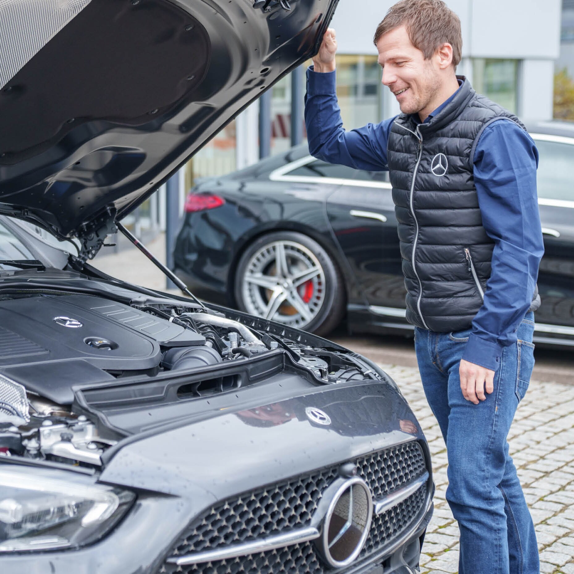 Uomo che osserva il motore di una Mercedes con il cofano aperto.