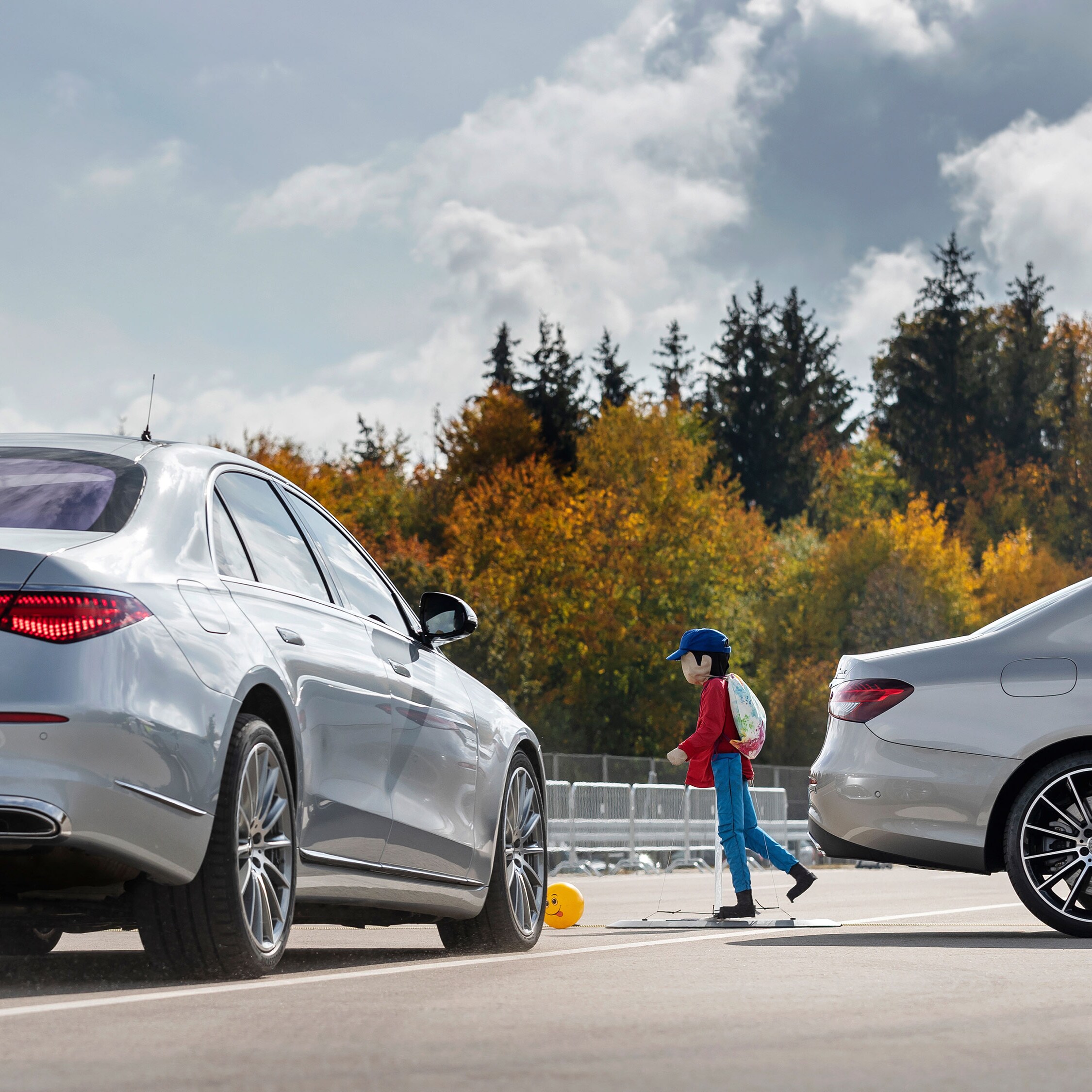 Zwei Mercedes-Benz Fahrzeuge und eine Fussgängerpuppe, die eine gefährliche Situation simulieren.