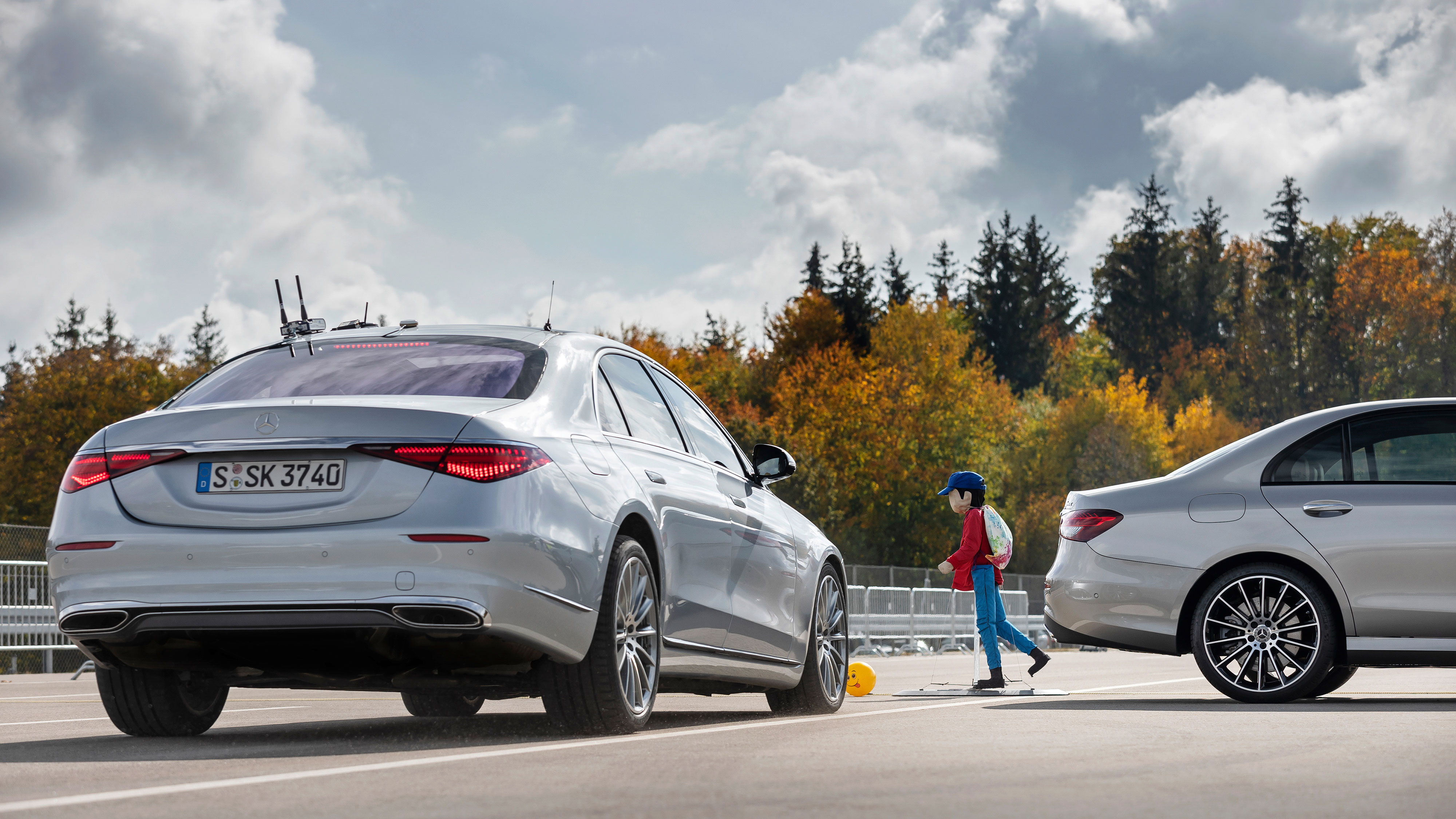 Zwei Mercedes-Benz Fahrzeuge und eine Fussgängerpuppe, die eine gefährliche Situation simulieren. Zwei Mercedes-Benz Fahrzeuge und eine Fussgängerpuppe, die eine gefährliche Situation simulieren.