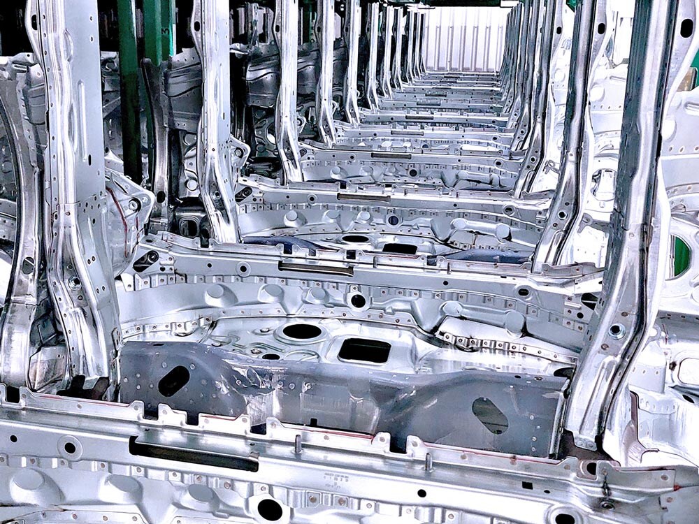 Plusieurs carrosseries de voitures en métal argenté sont alignées dans un atelier de production