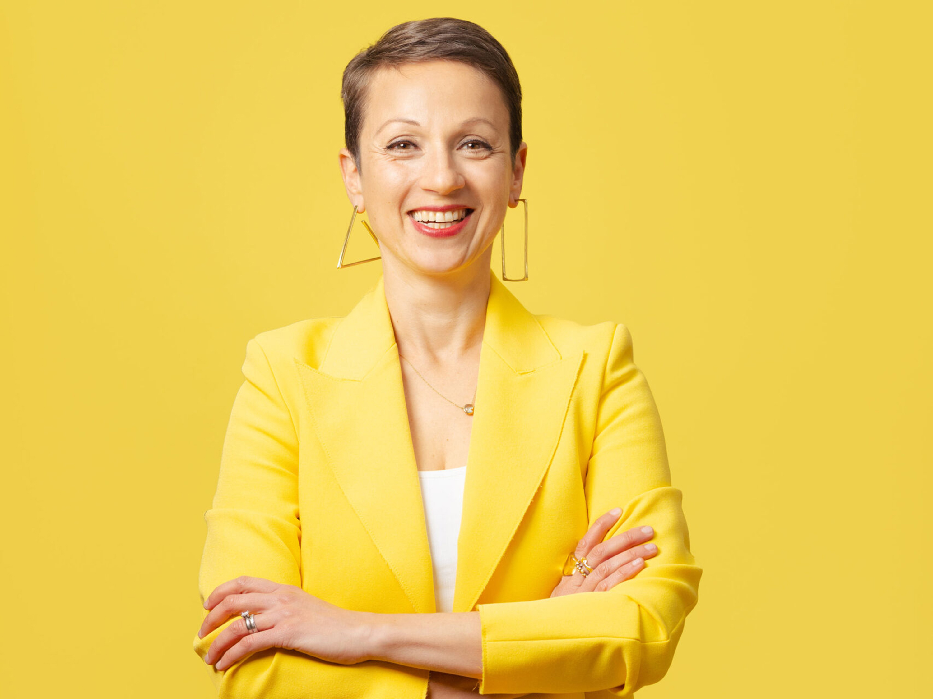 Nataly Kogan Smiling woman names Nataly Kogan in a yellow blazer standing against a yellow background.