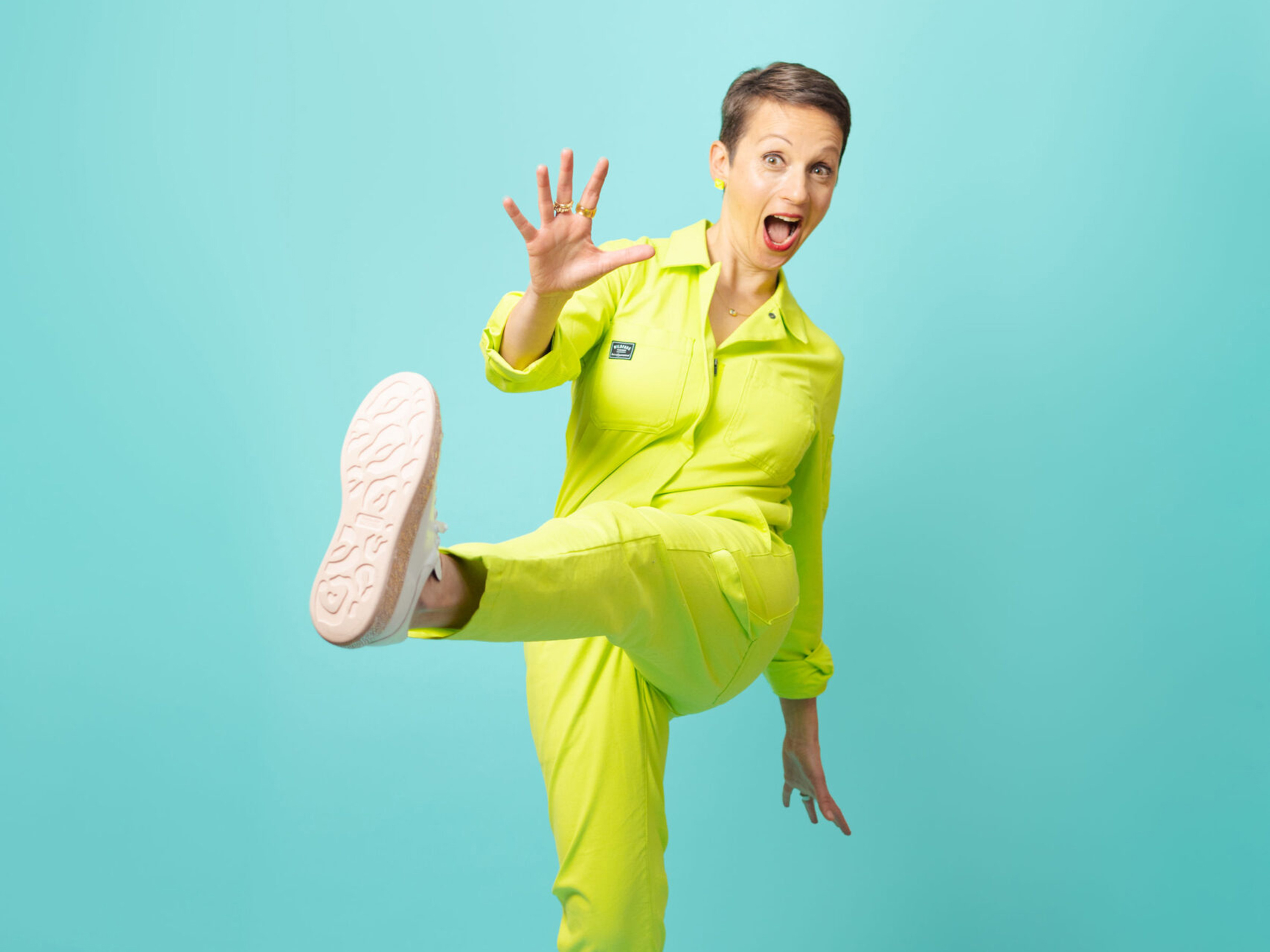 Nataly Kogan Nataly Kogan en tenue fluo faisant un coup de pied ludique sur fond turquoise.