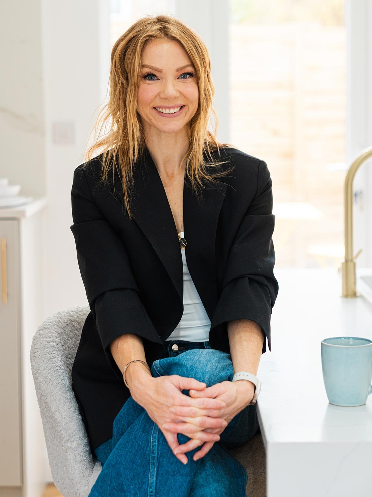 Vêtue d'un blazer noir, Jessica Barac est assise sur une chaise dans un appartement.