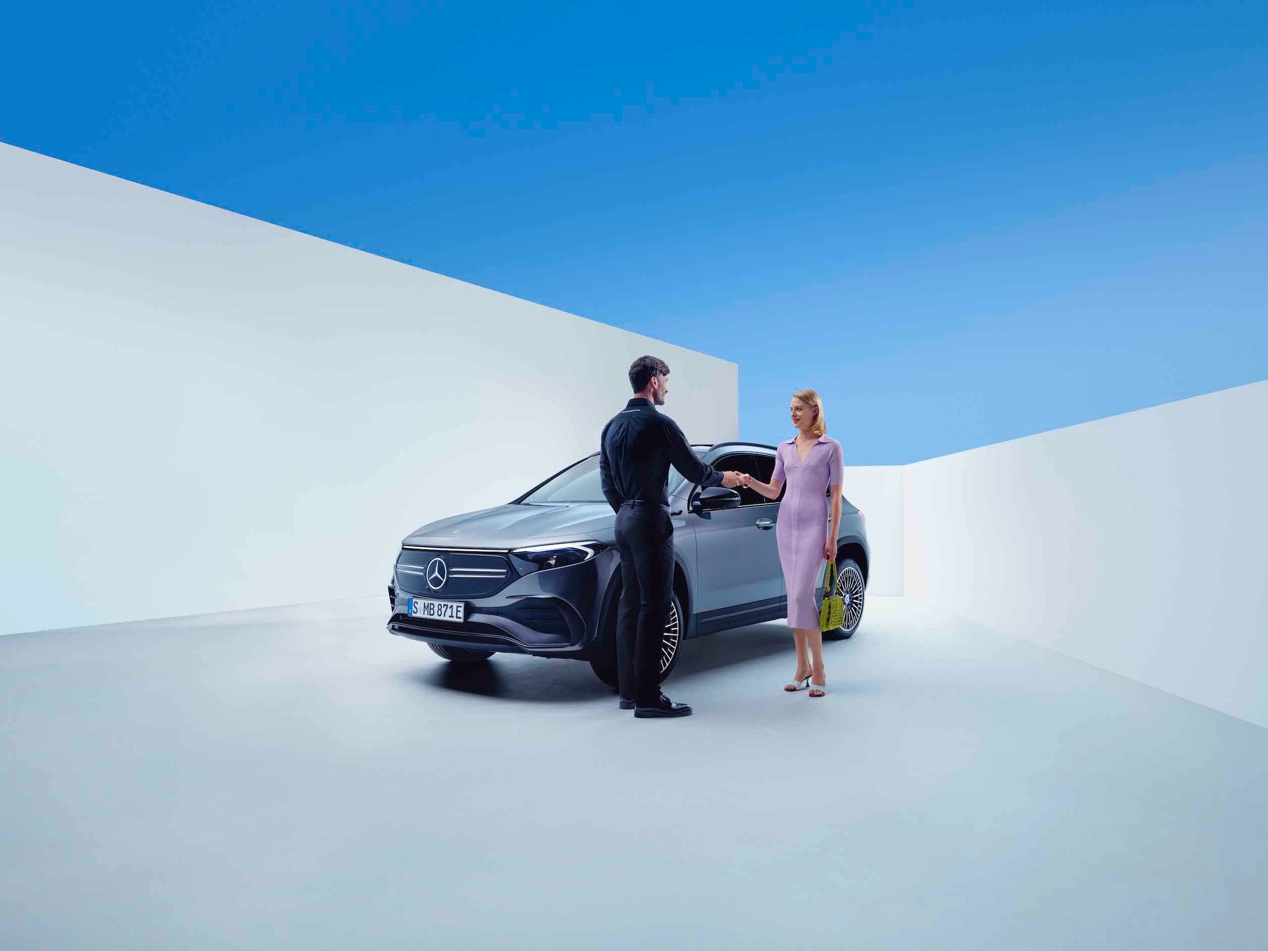 Donna e uomo si stringono la mano davanti a una Mercedes-Benz grigia