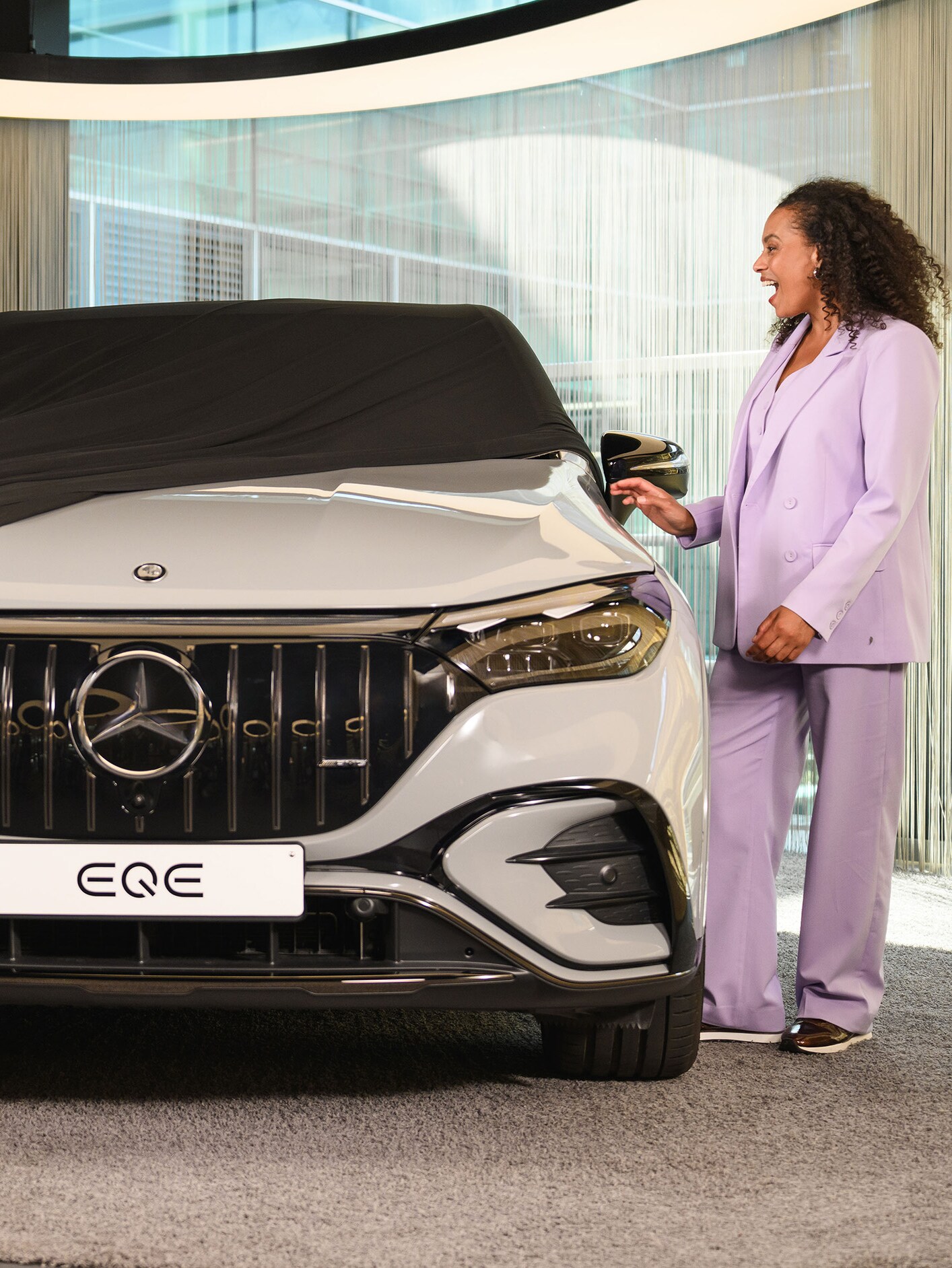 Zwei Personen und ein Kind, die in einem Showroom eine Abdeckung von einem neuen Mercedes-Benz Fahrzeug entfernen.