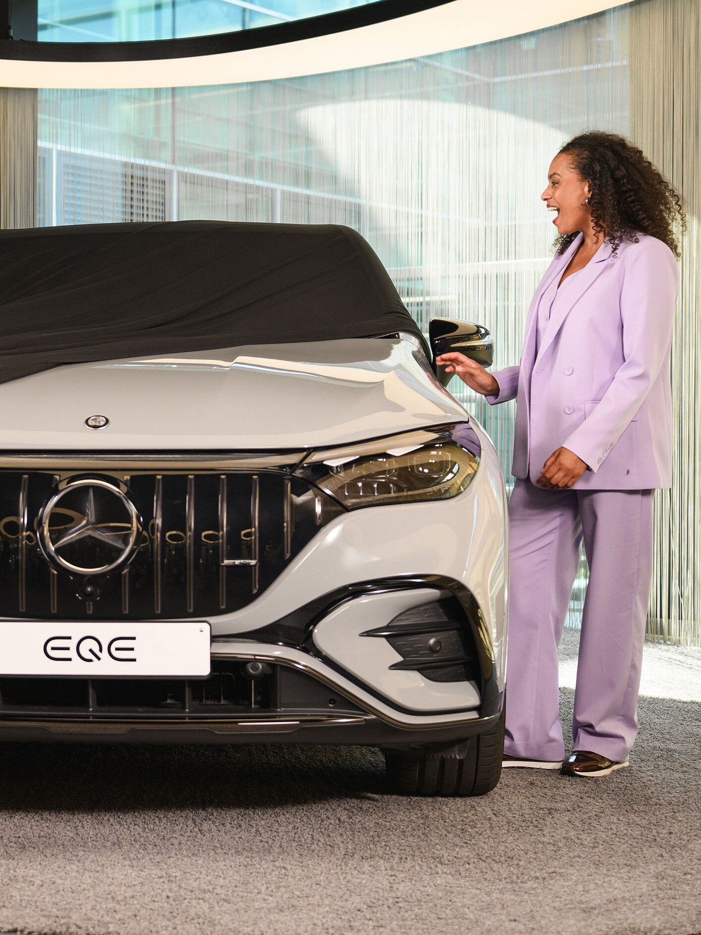 Due persone e un bambino tolgono un telo di copertura da una nuova Mercedes-Benz in uno showroom.​