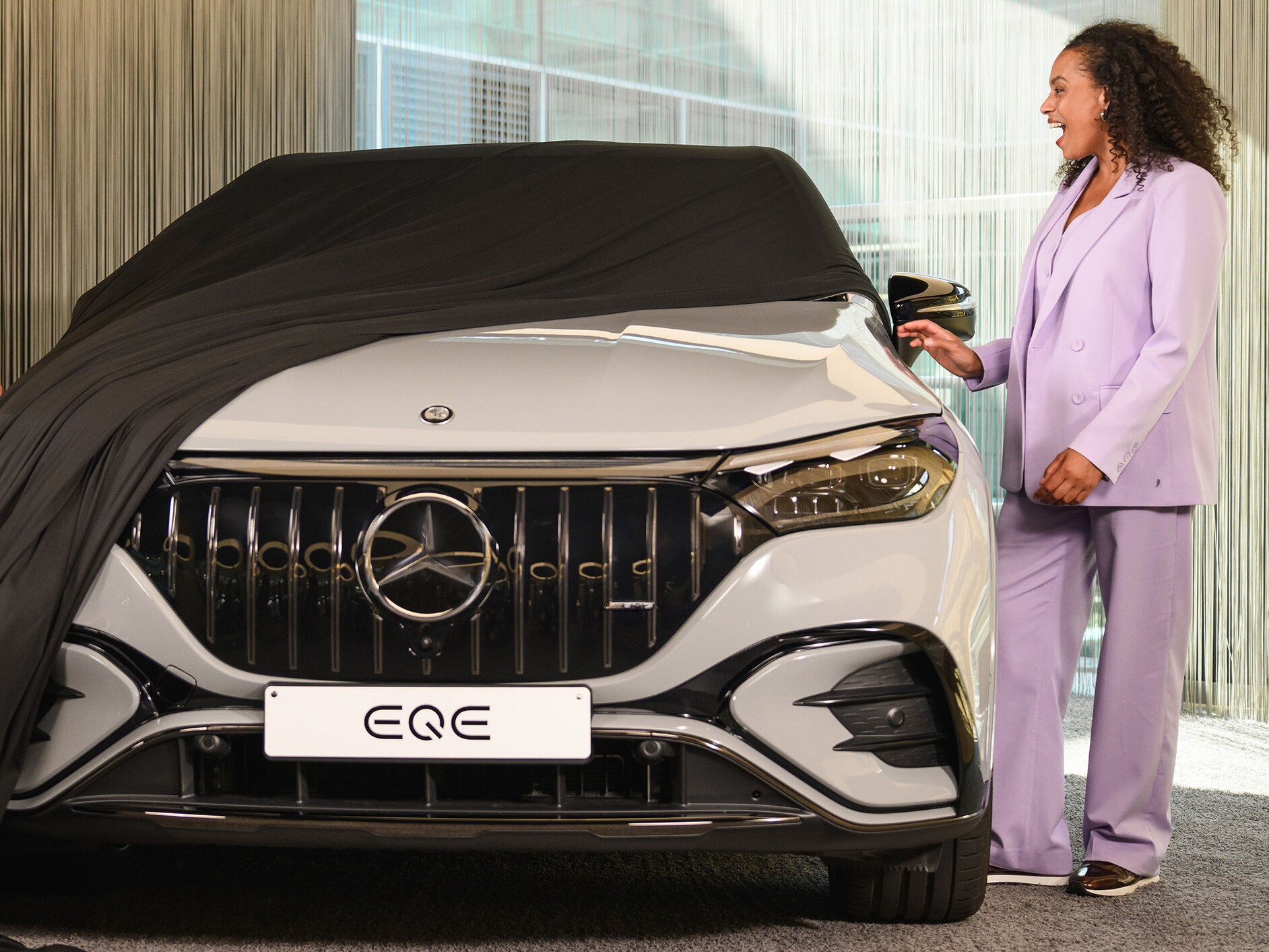 Femme dévoilant une Mercedes-Benz EQE dans un showroom.
