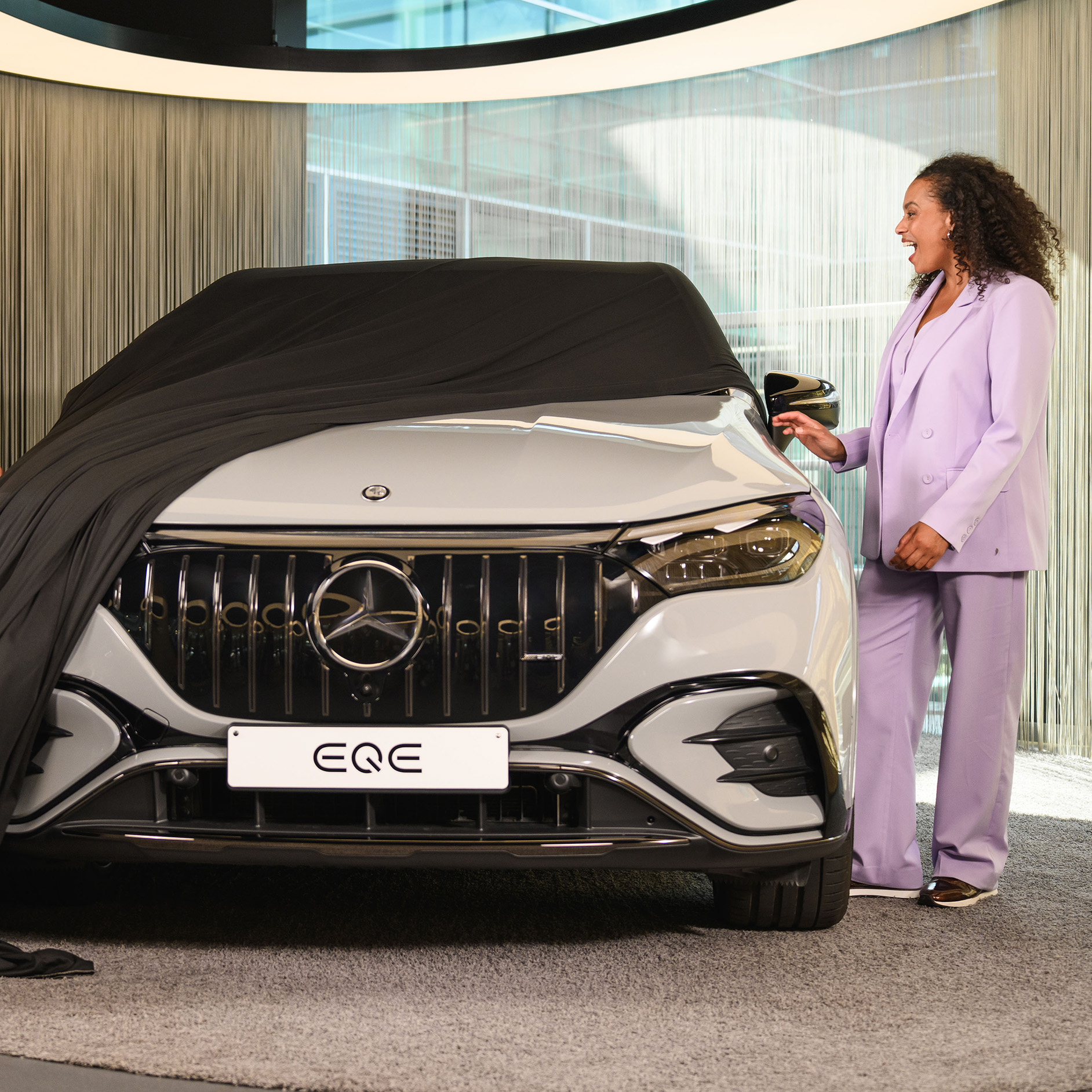 Offres de leasing pour véhicules neufs Mercedes-Benz. Femme dévoilant une Mercedes-Benz EQE dans un showroom.