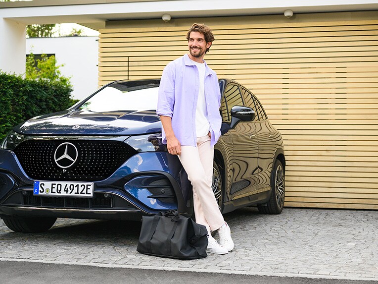 Une personne appuyée contre un véhicule Mercedes-Benz devant sa maison.