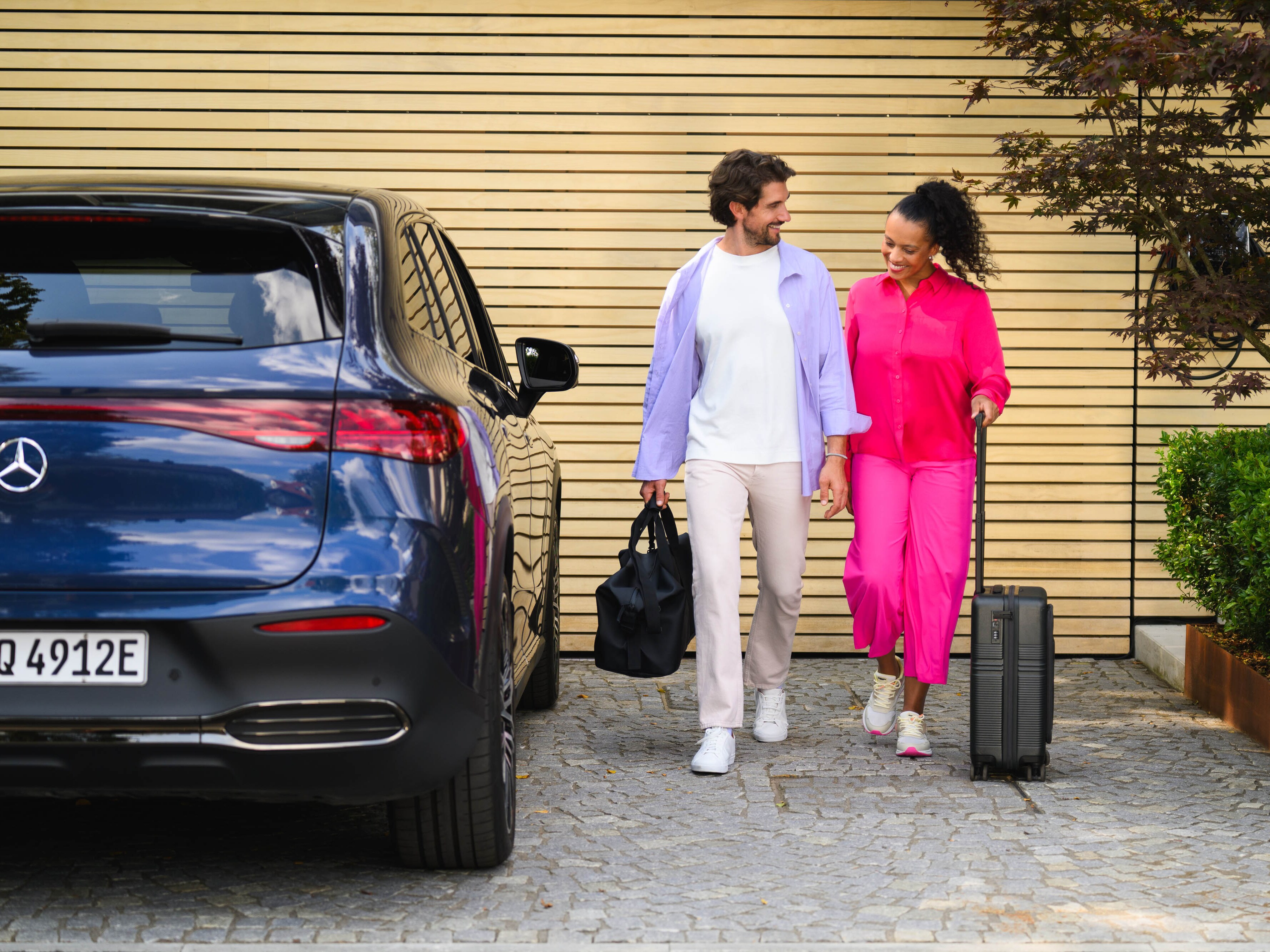 Deux personnes marchant vers un véhicule Mercedes-Benz,  l’un avec une valise et l’autre tenant un sac de sport.