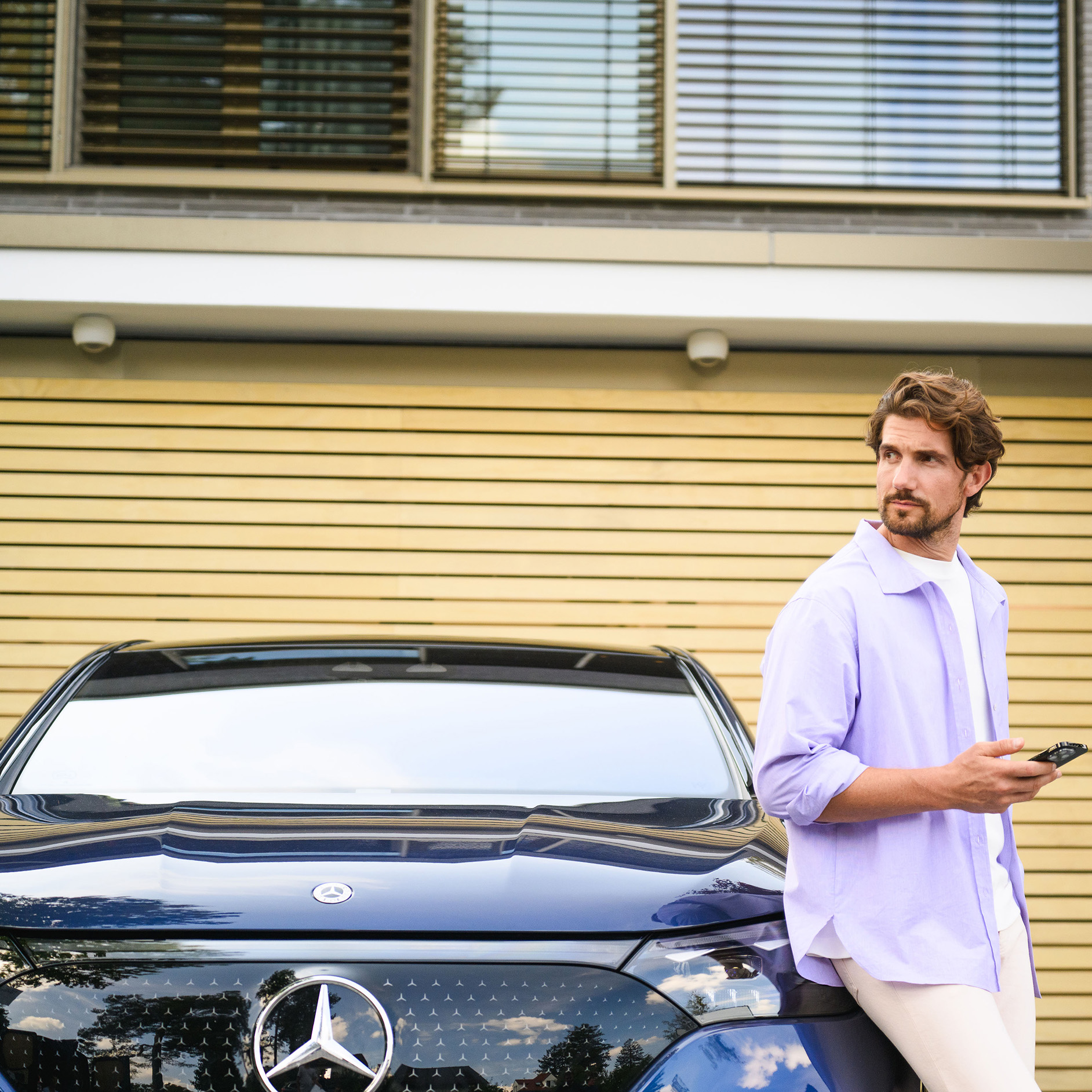 Offerte di leasing per veicoli d’occasione Mercedes-Benz Una persona è appoggiata a una Mercedes-Benz, guarda lontano e tiene in mano un dispositivo mobile.