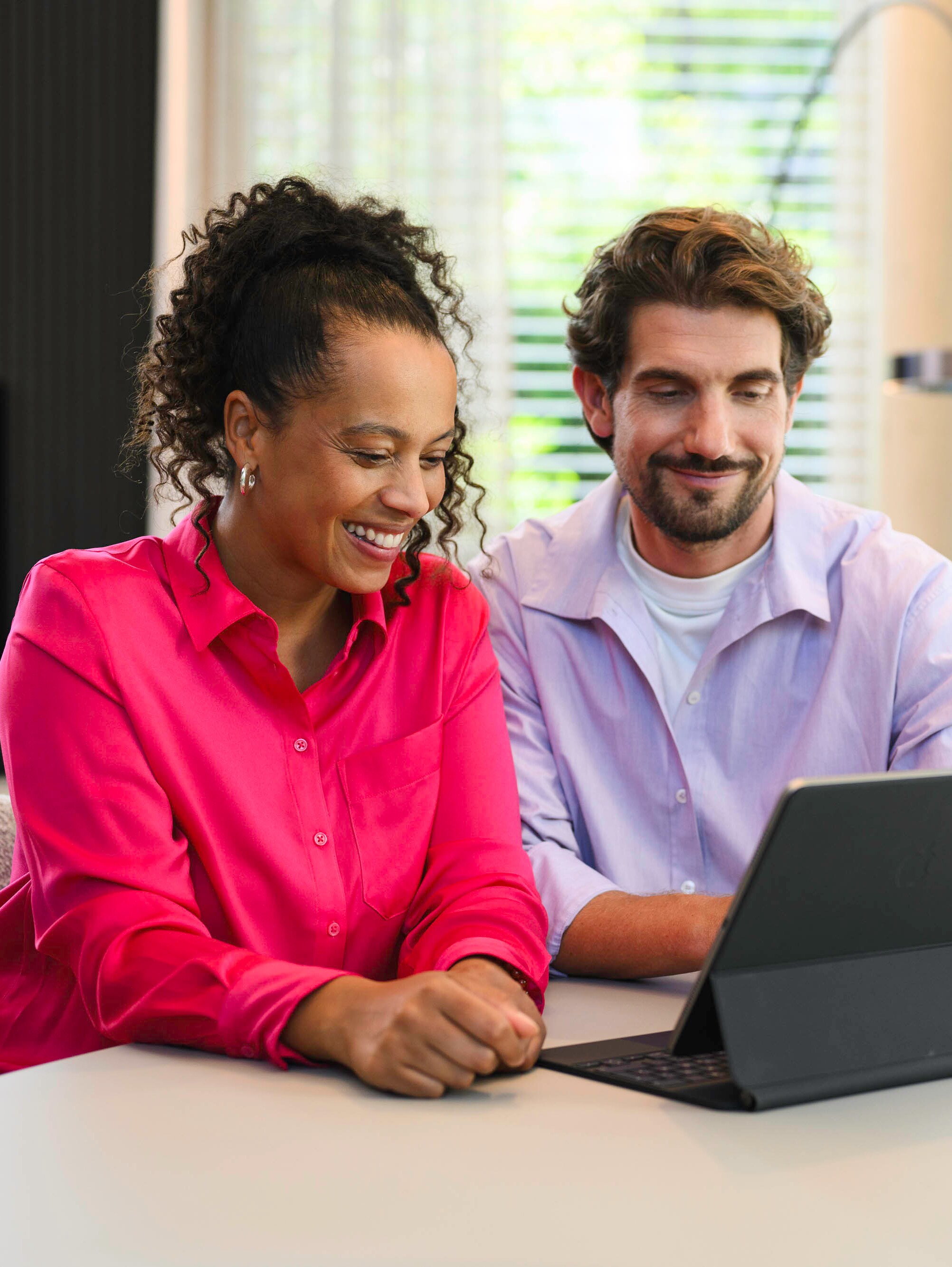Due persone sono sedute a un tavolo e guardano un dispositivo mobile.