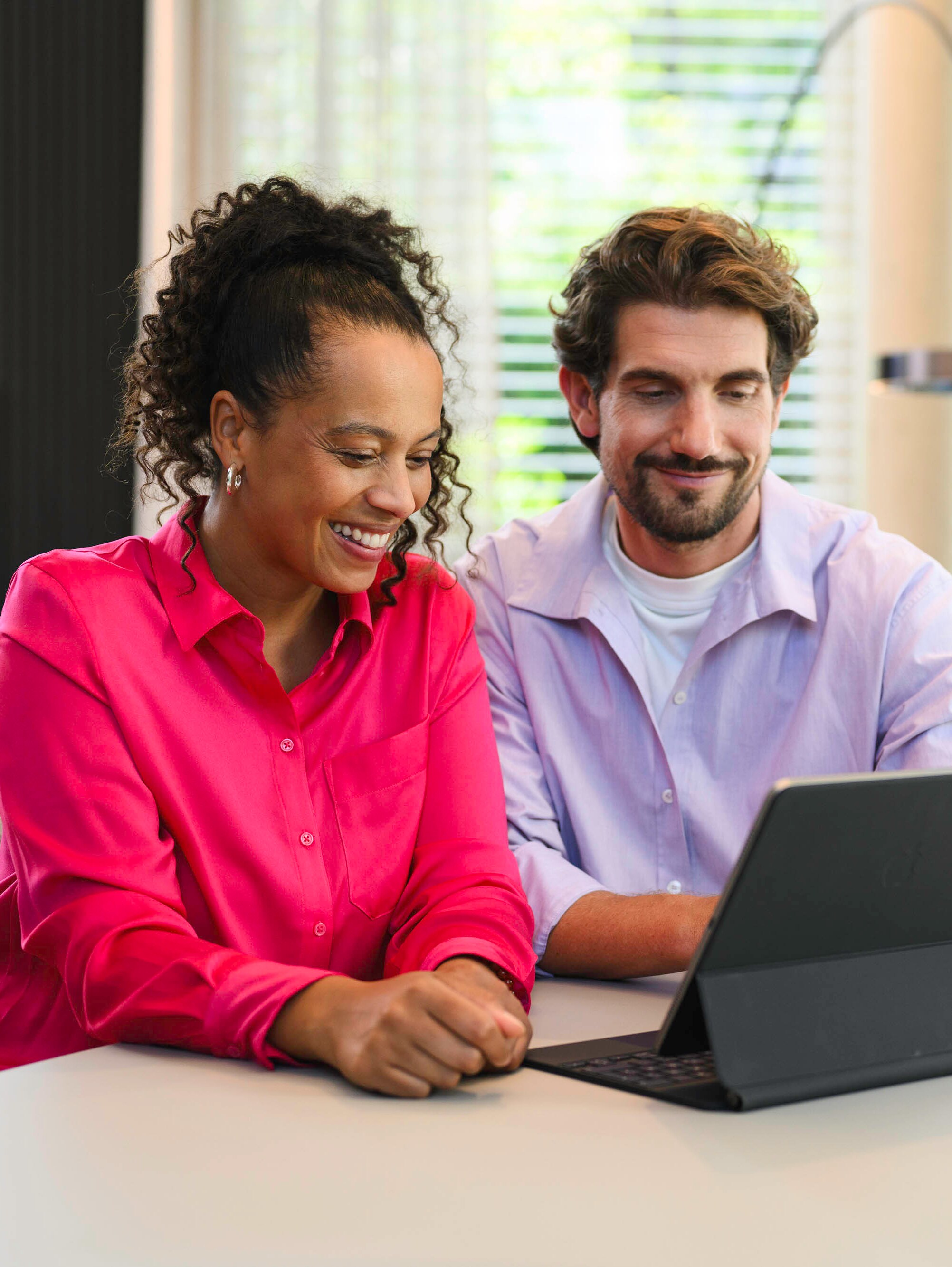 Zwei Personen sitzen an einem Tisch und schauen auf ein mobiles Gerät.