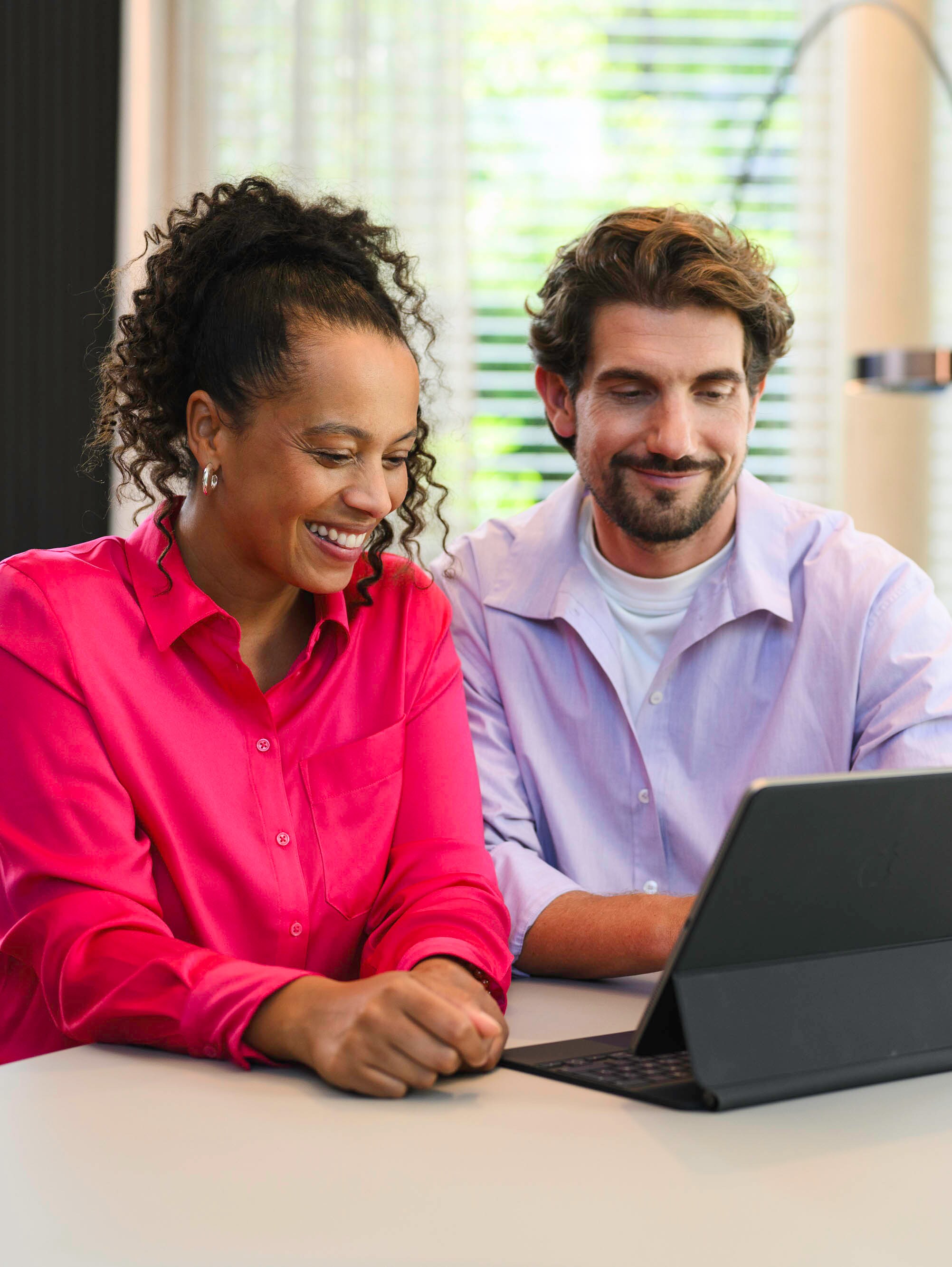 Zwei Personen sitzen an einem Tisch und schauen auf ein mobiles Gerät.