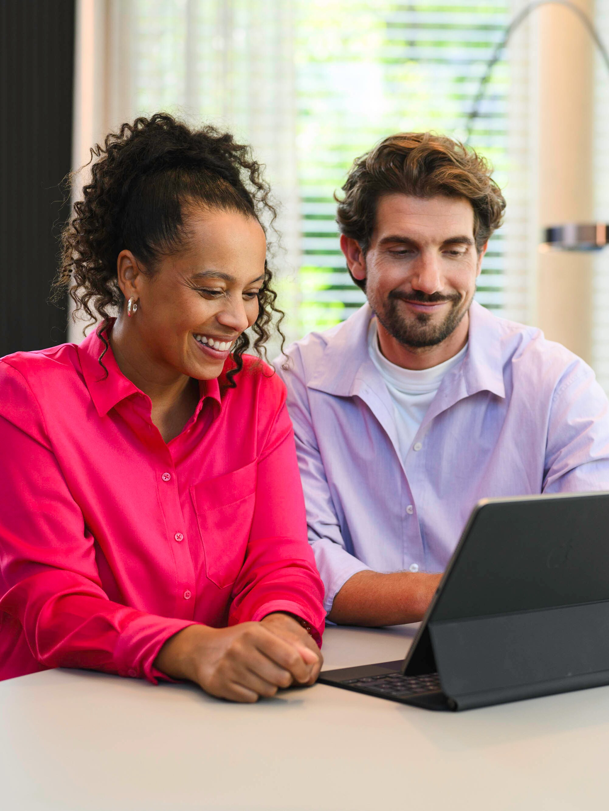 Zwei Personen sitzen an einem Tisch und schauen auf ein mobiles Gerät.