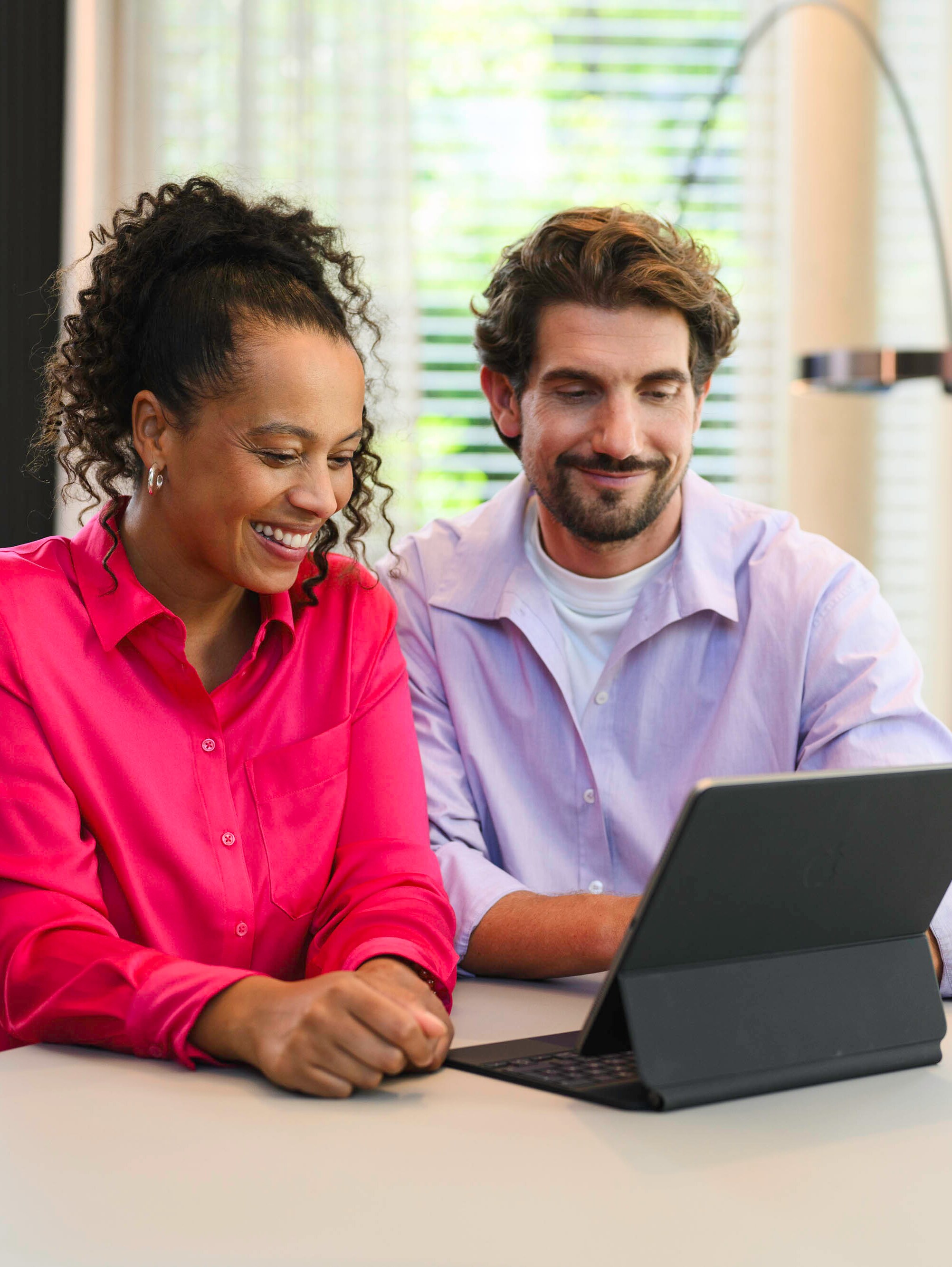 Zwei Personen sitzen an einem Tisch und schauen auf ein mobiles Gerät.