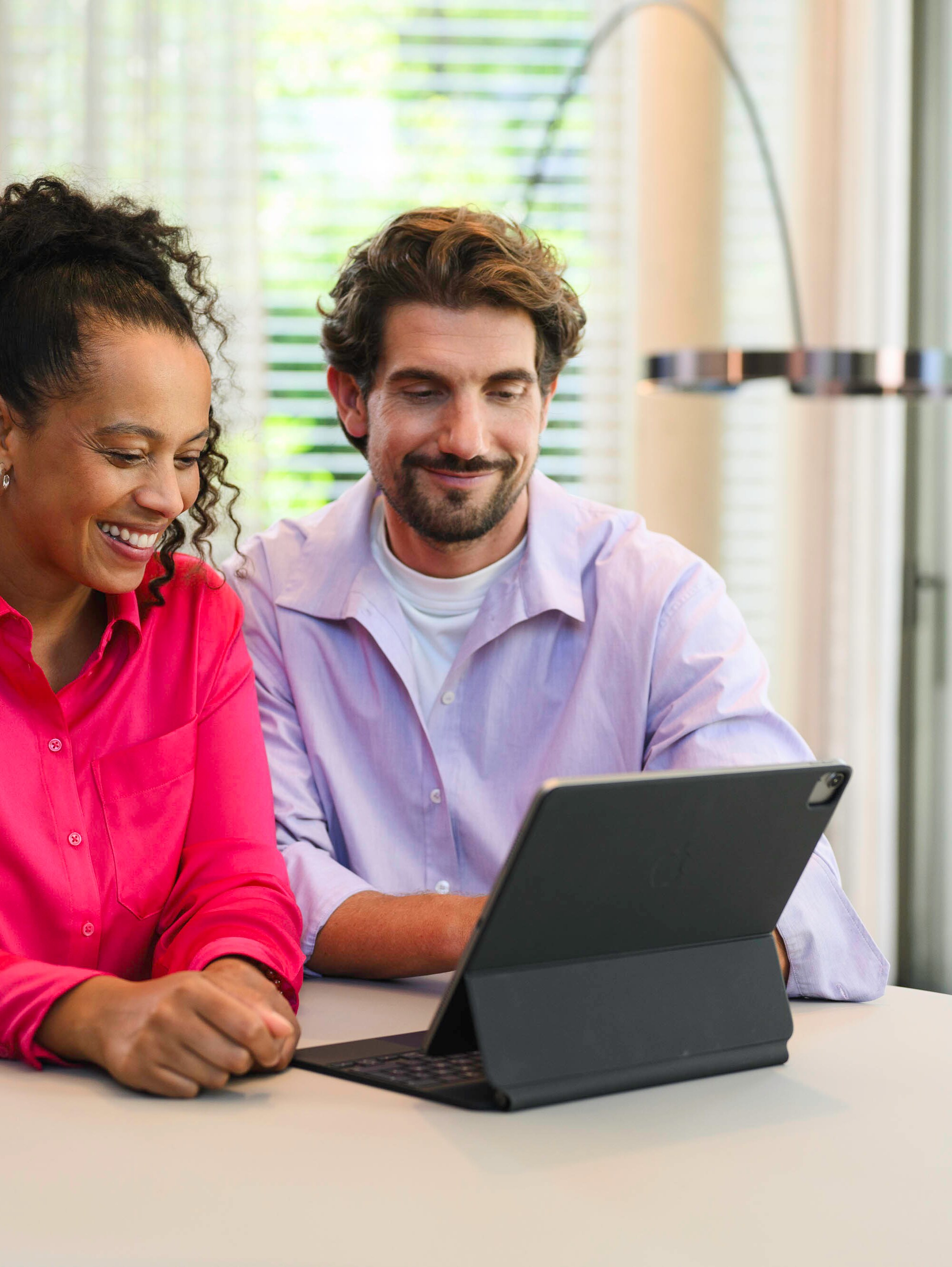Due persone sono sedute a un tavolo e guardano un dispositivo mobile.