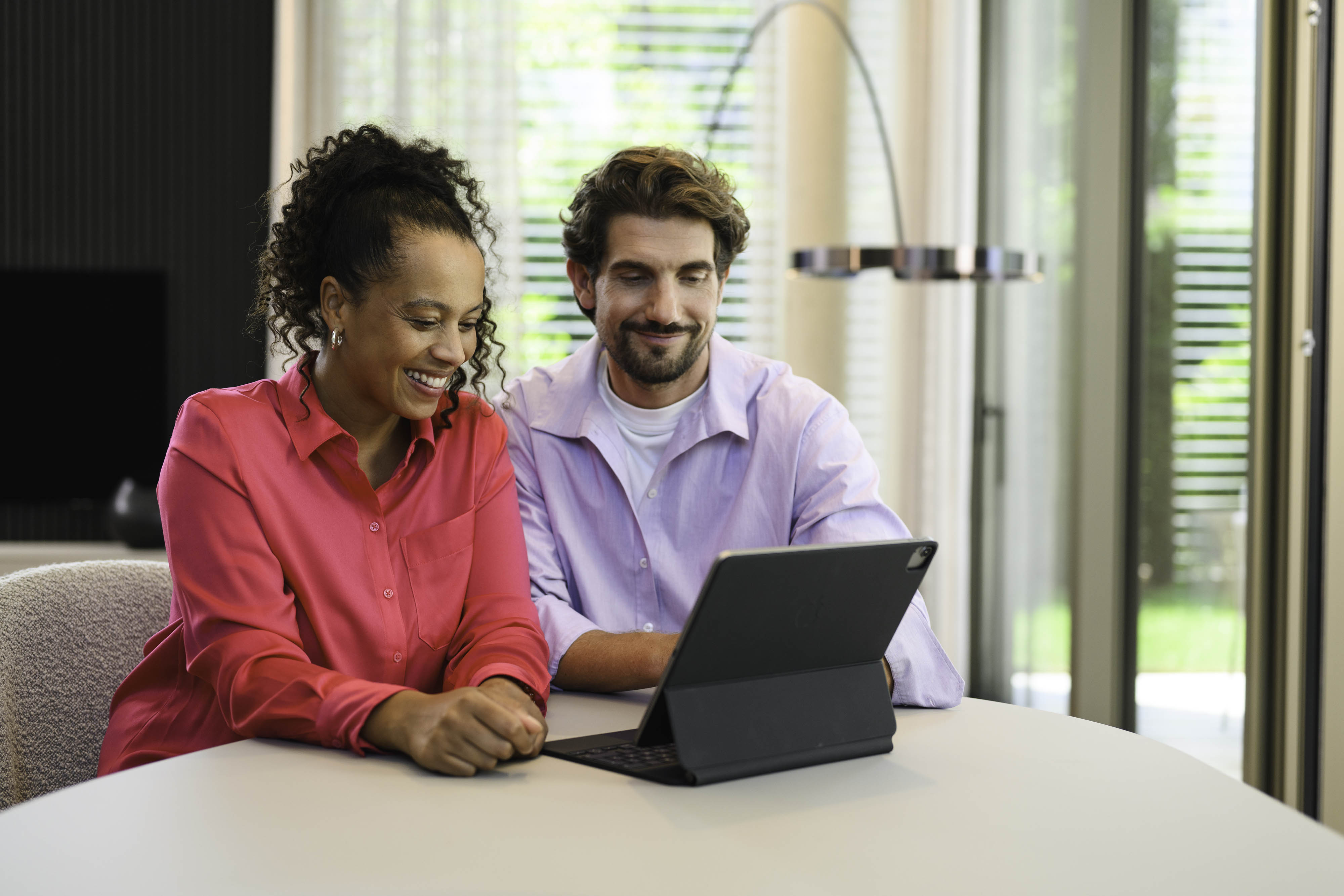 Mercedes-Benz Finance Kundenportal Zwei Personen sitzen an einem Tisch und schauen auf ein mobiles Gerät.
