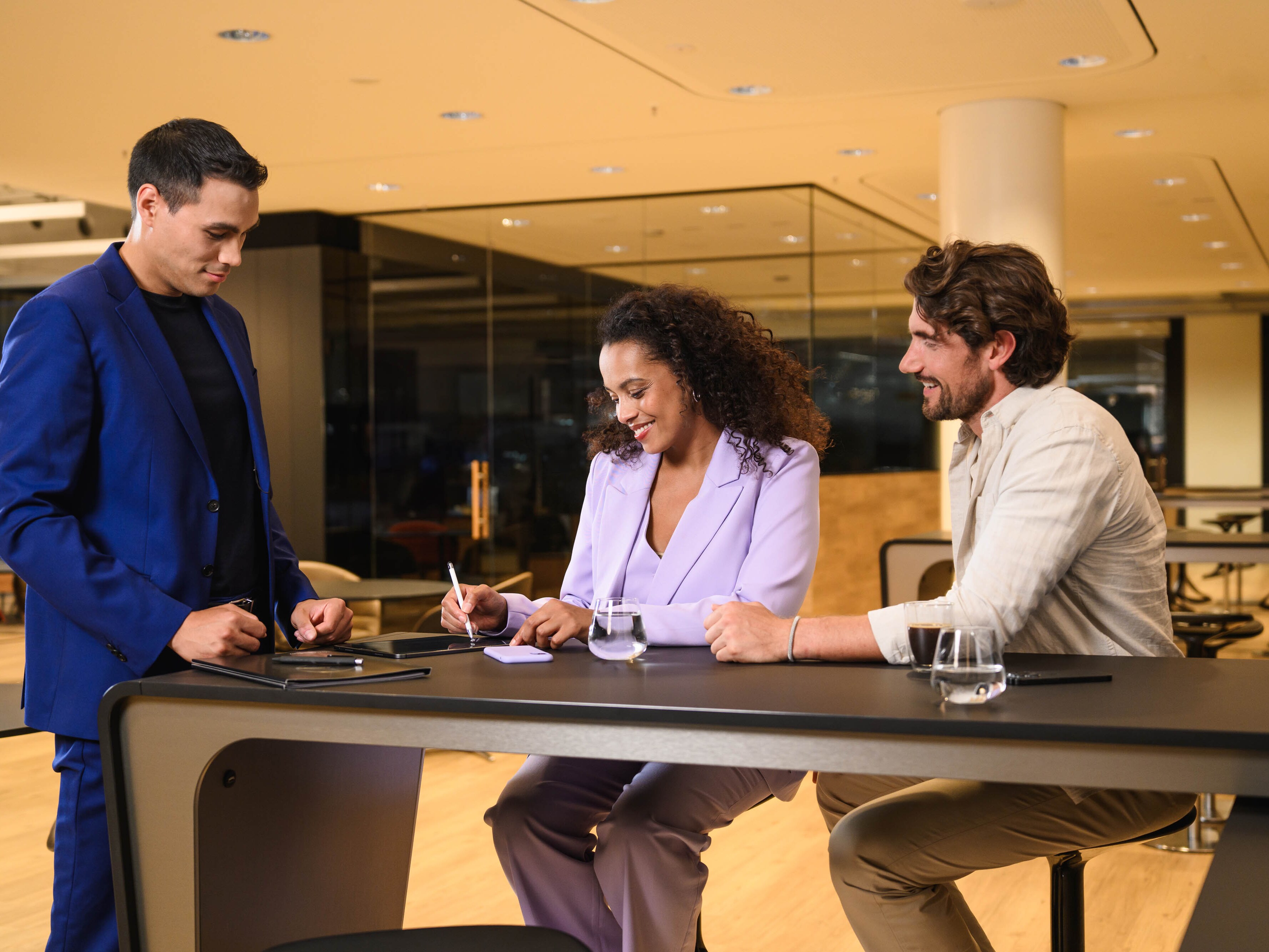 Une personne signe un document à une table et deux autres personnes sont présentes.