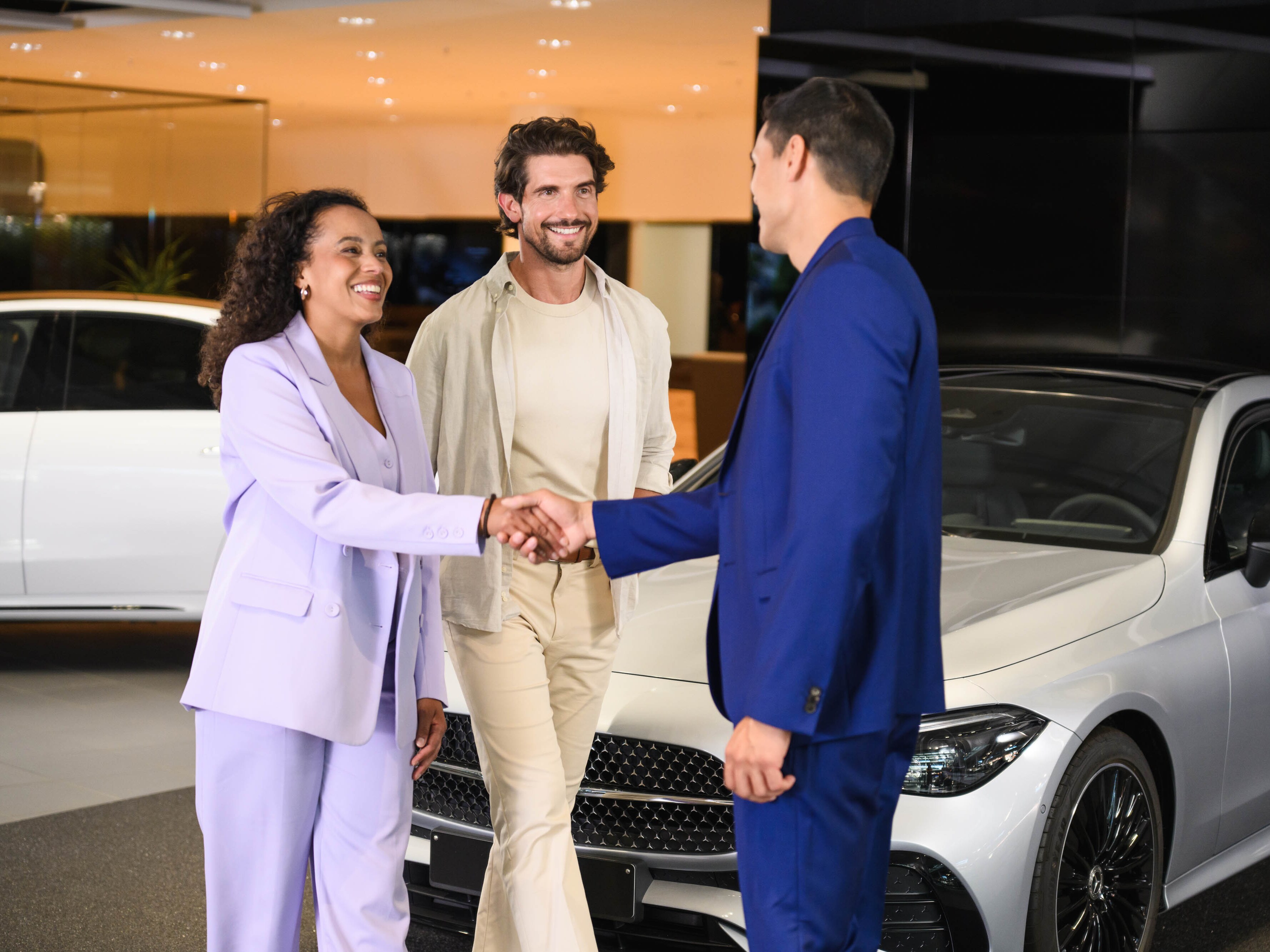 Trois personnes se présentent devant une Mercedes-Benz, deux d'entre elles se serrent la main.