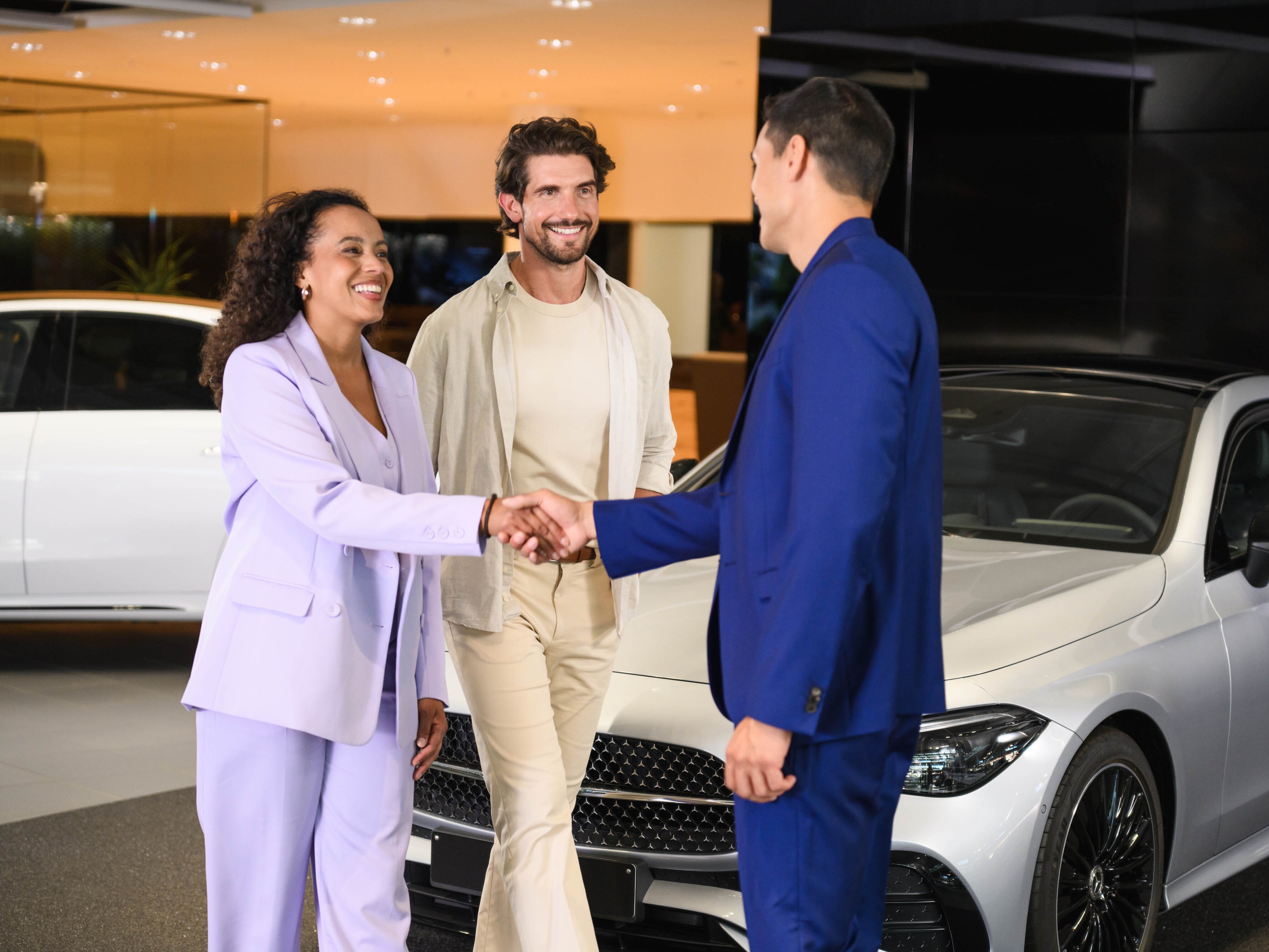 Drei Personen stehen vor einem Mercedes-Benz, zwei davon schütteln sich die Hände.