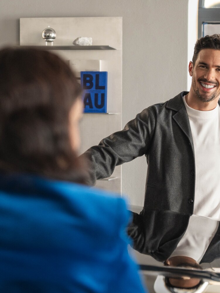 Zwei Personen lehnen sich an eine Motorhaube eines Mercedes-Benz und unterhalten sich.
