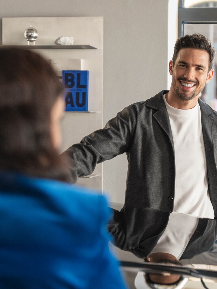 Zwei Personen lehnen sich an eine Motorhaube eines Mercedes-Benz und unterhalten sich.