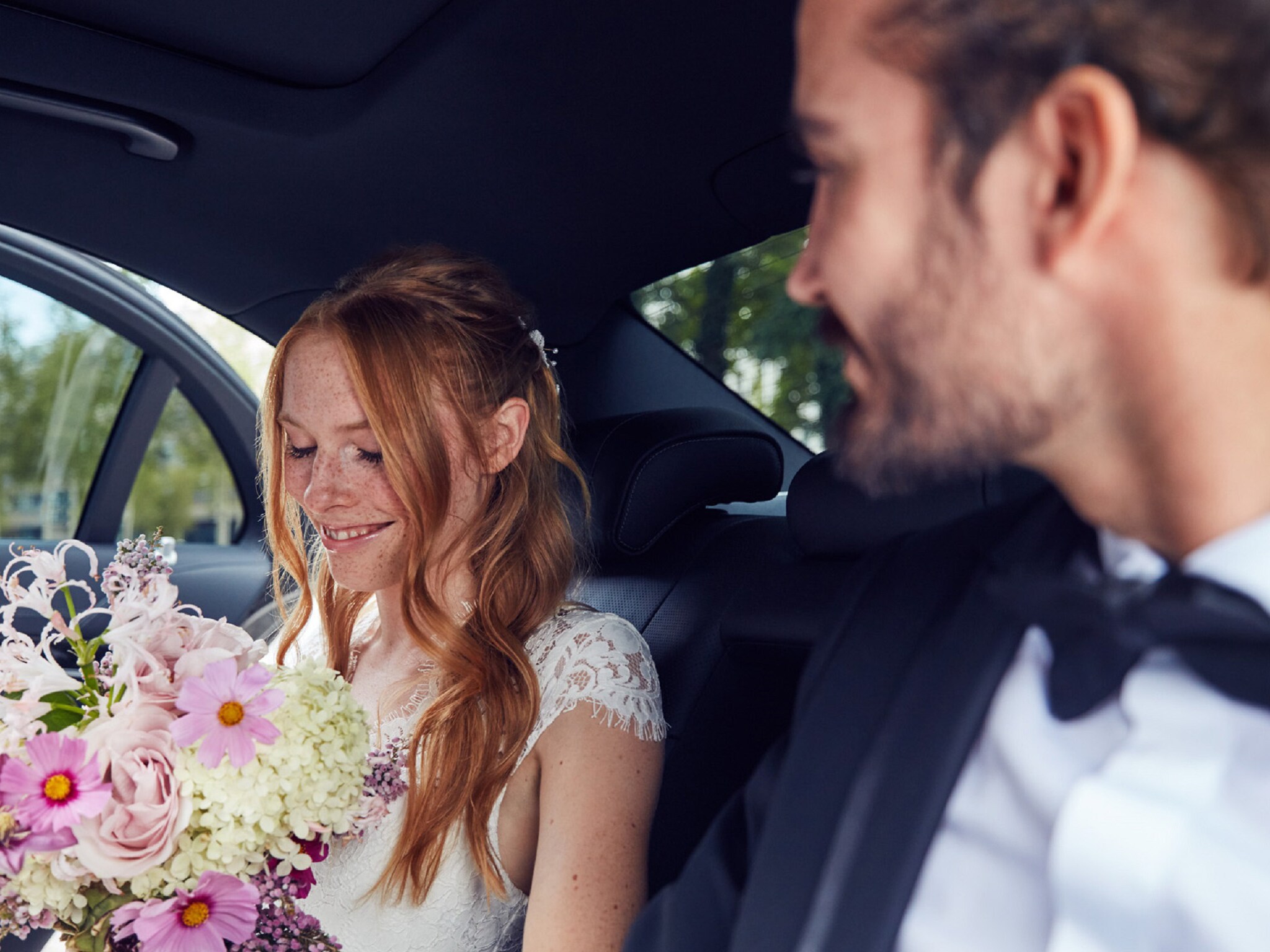Brautpaar sitzt hinten in einer Mercedes-Benz Limousine mit einem Blumenstrauss.