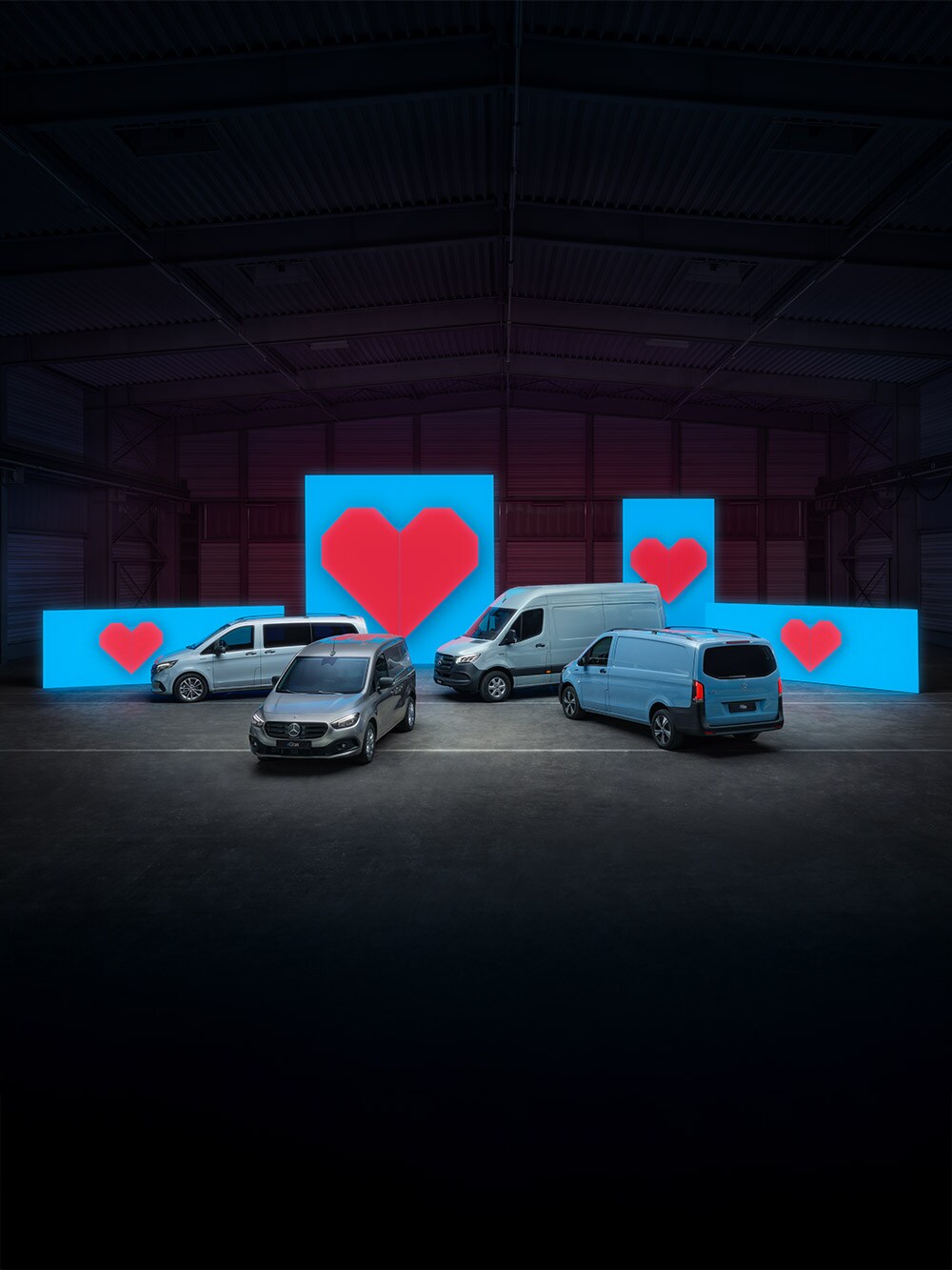 Vari modelli di van elettrici si trovano davanti a pareti illuminate di blu, ognuno con un cuore rosso.