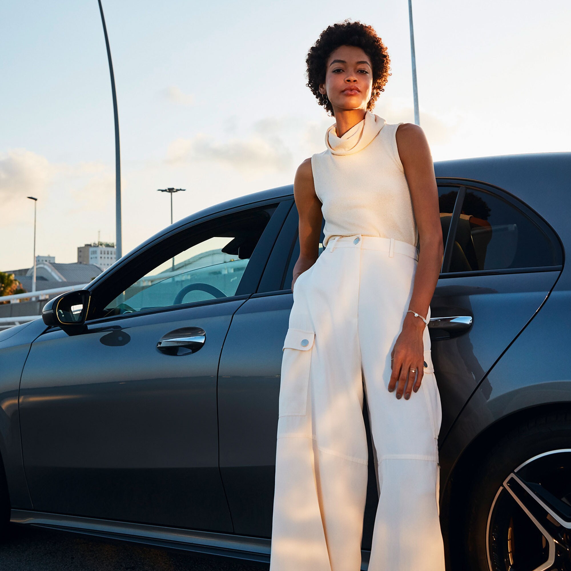 Une femme est adossée à une Mercedes-Benz et regarde l'objectif.