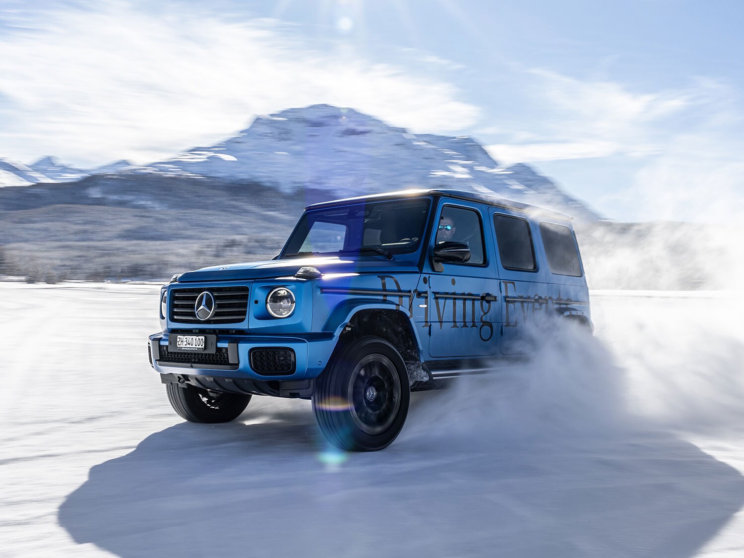 Mercedes-Benz G-Klasse fährt auf verschneiter Fläche vor Bergkulisse.