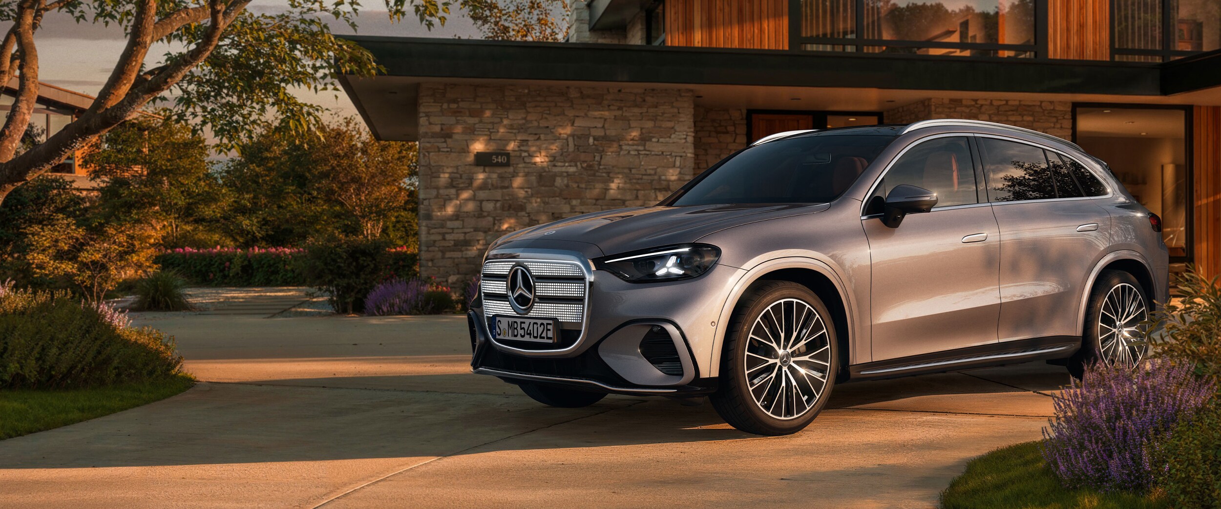 SUV Mercedes argenté devant une maison moderne au crépuscule.