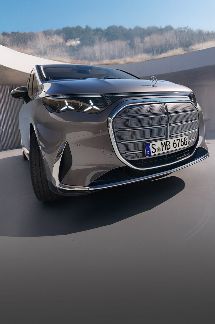 Gezeigt wird der VLE von Mercedes-Benz. Parkend vor einem modernem Gebäude mit einem Kirschbaum an der Seite.