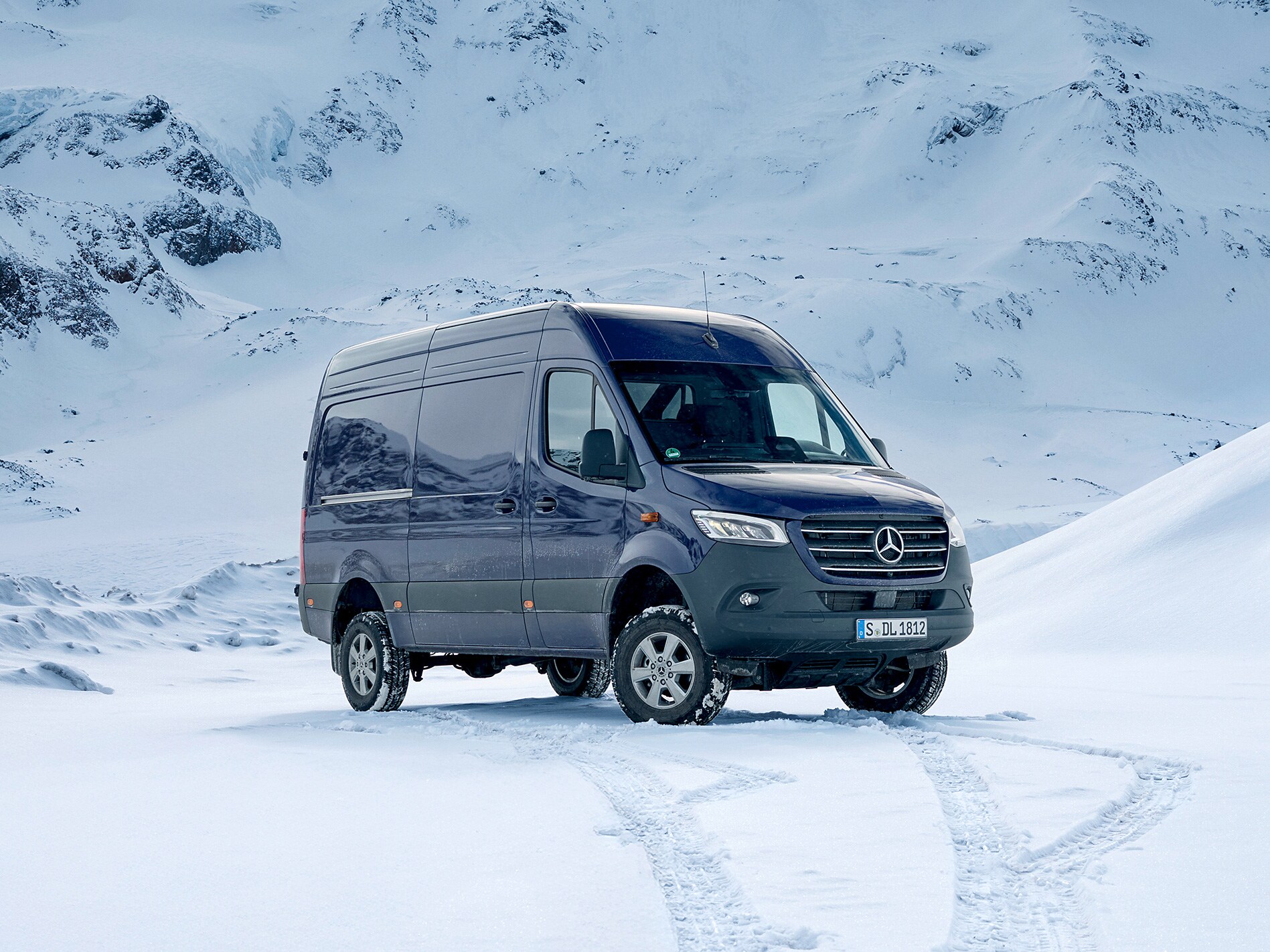 Un Mercedes-Benz Sprinter blu scuro è fermo nella neve davanti a un panorama montano innevato.