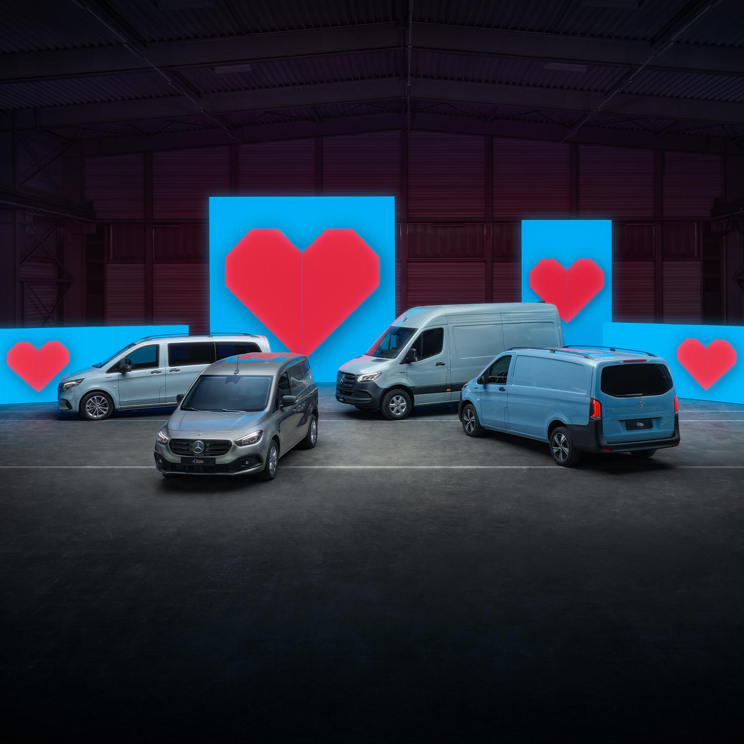 Verschiedene Van-Elektromodelle stehen vor blauen Leuchtwänden mit je einem roten Herz.