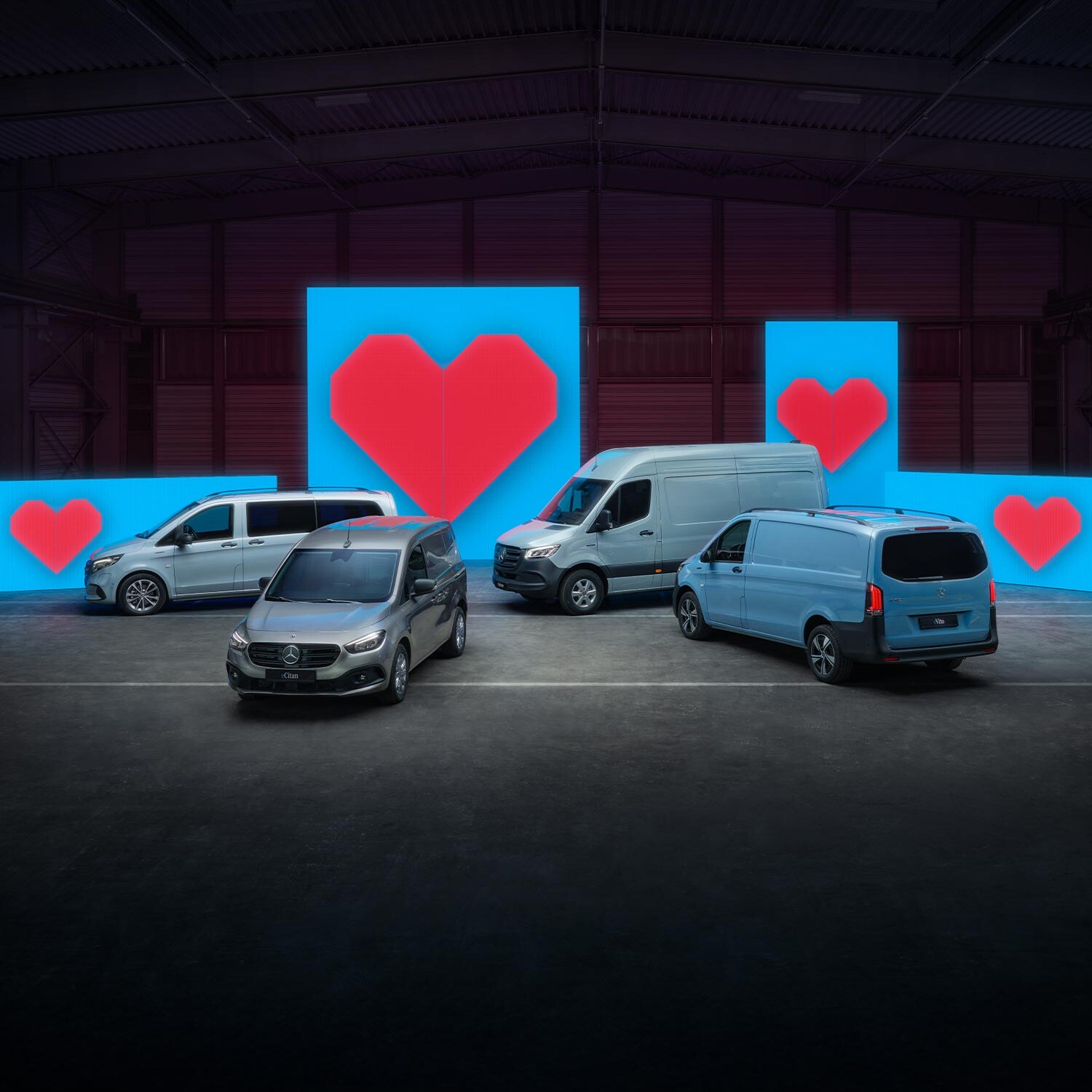 Verschiedene Van-Elektromodelle stehen vor blauen Leuchtwänden mit je einem roten Herz.
