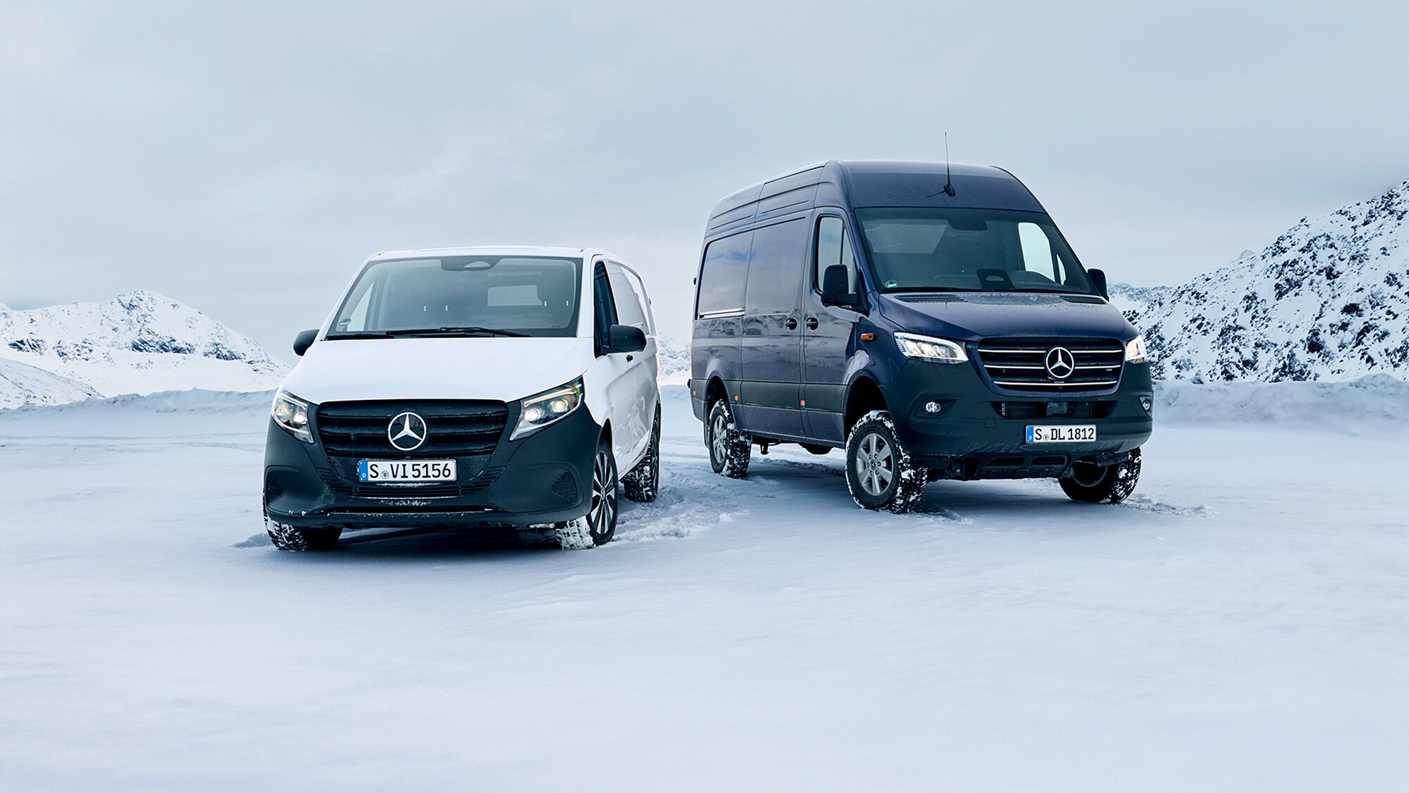 Un Mercedes-Benz Vito bianco e un Mercedes-Benz Sprinter blu scuro sono parcheggiati su un prato innevato in montagna.