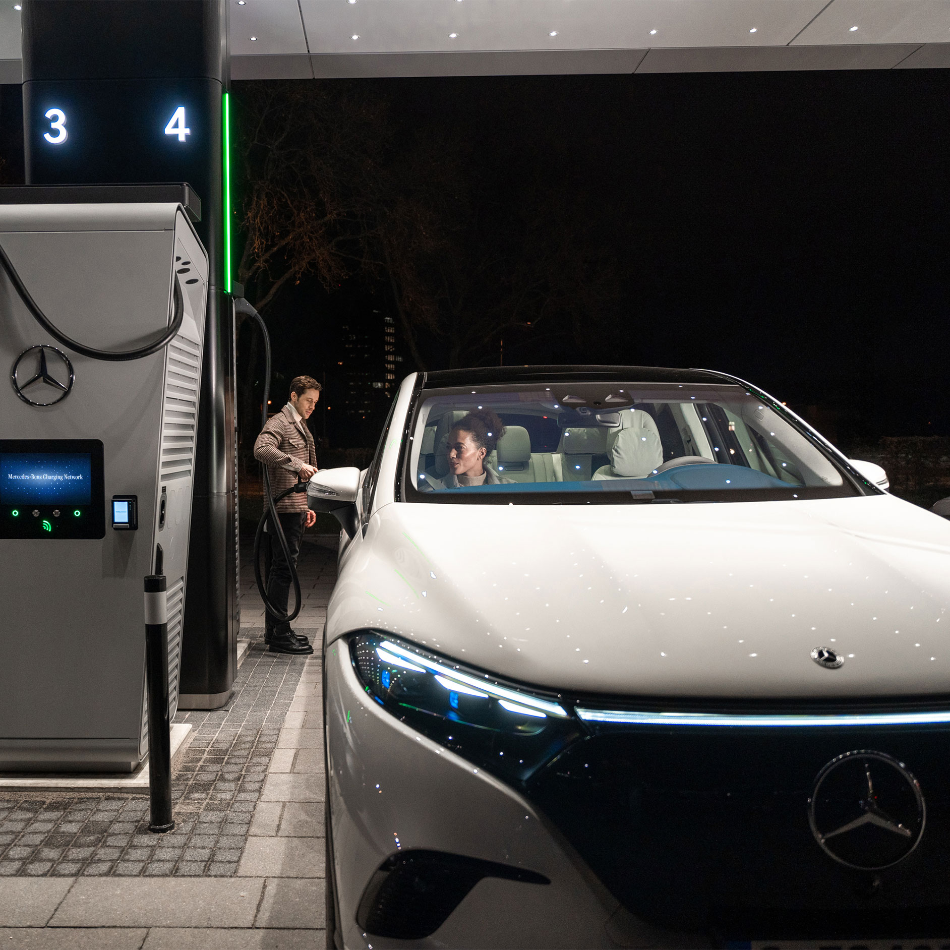 Ladelösungen | Technik | Mercedes-Benz Der Mercedes-Benz CLA steht auf einer Straße, angeschlossen an eine Ladestation.