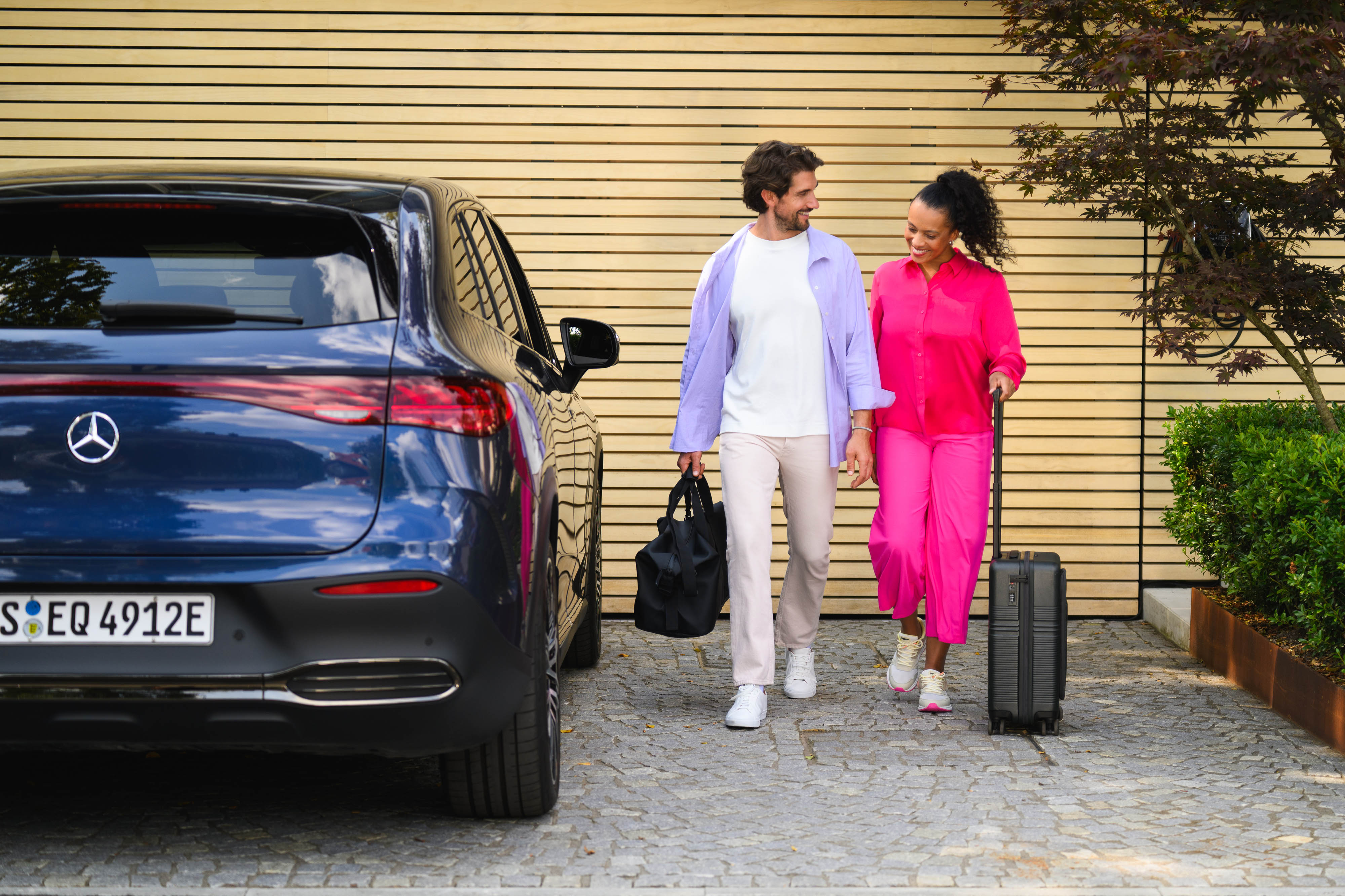 Attraktive Leasingangebote entdecken Zwei Personen gehen auf einen Mercedes-Benz zu, eine mit einem Koffer und die andere mit einer Sporttasche.